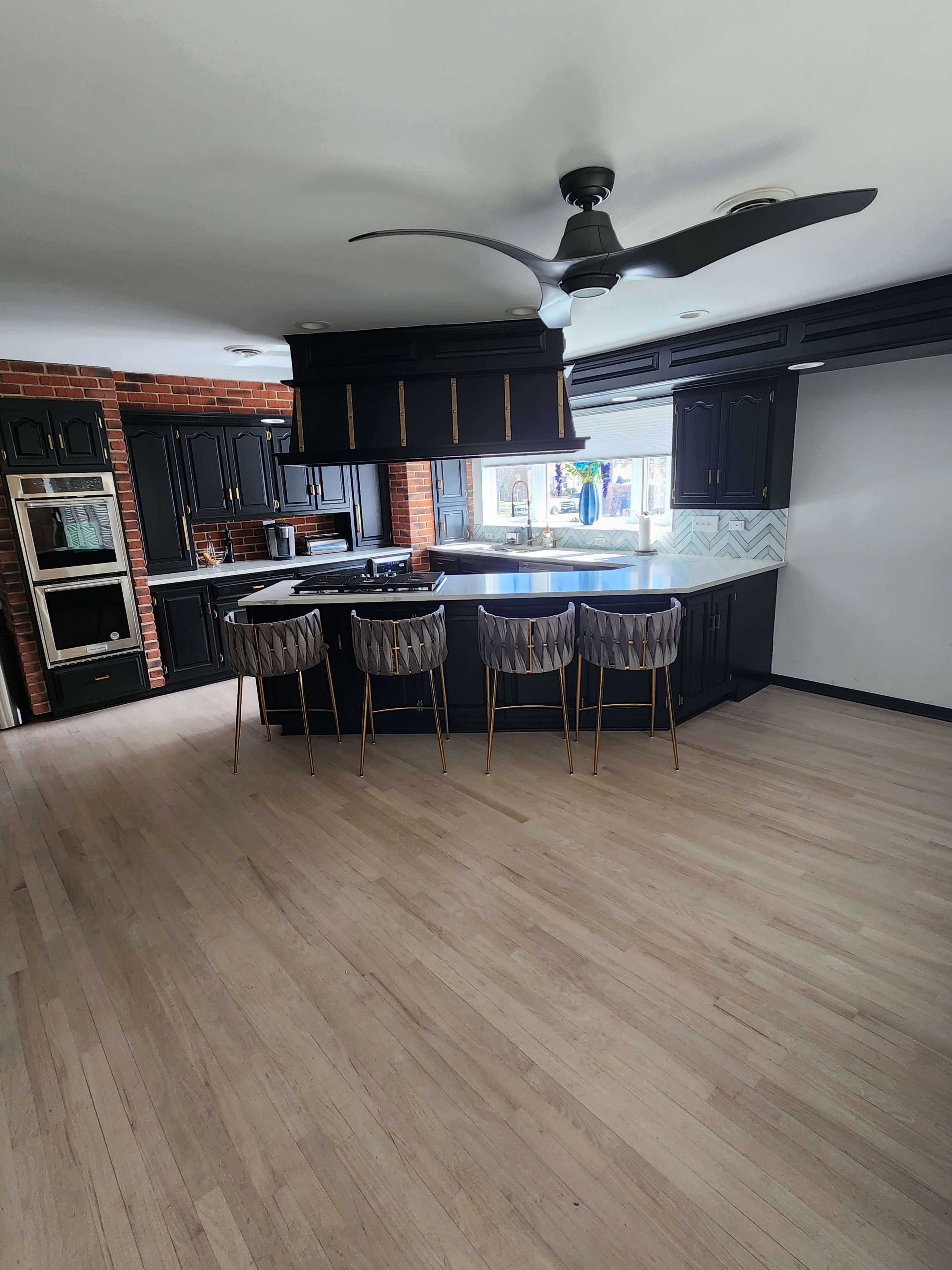 A modern kitchen features black cabinetry, a central island with a countertop, and four bar stools arranged around it.