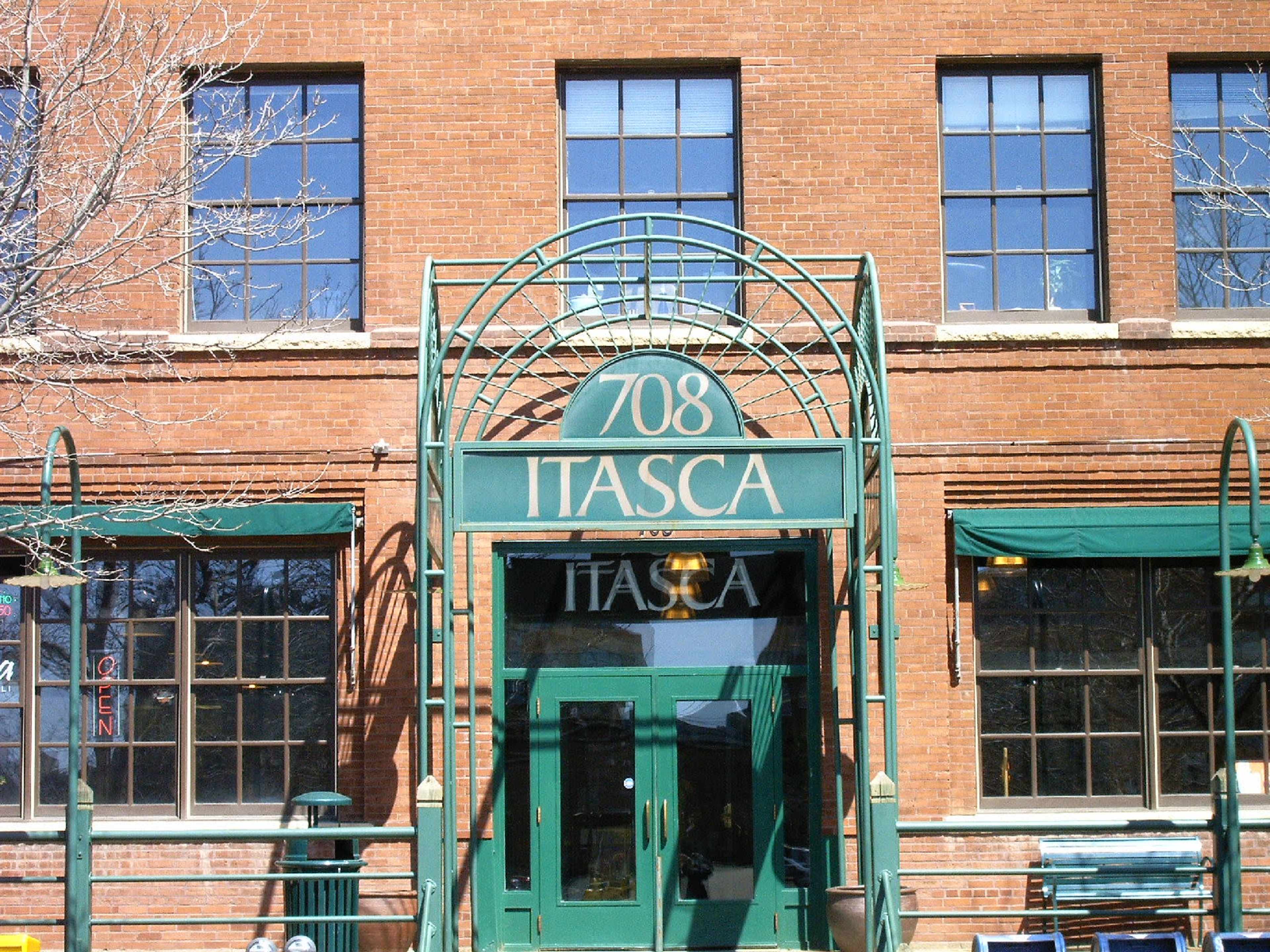 The image shows a brick building with large windows and a green entrance featuring the name "ITASCA" and the number "708" prominently displayed.