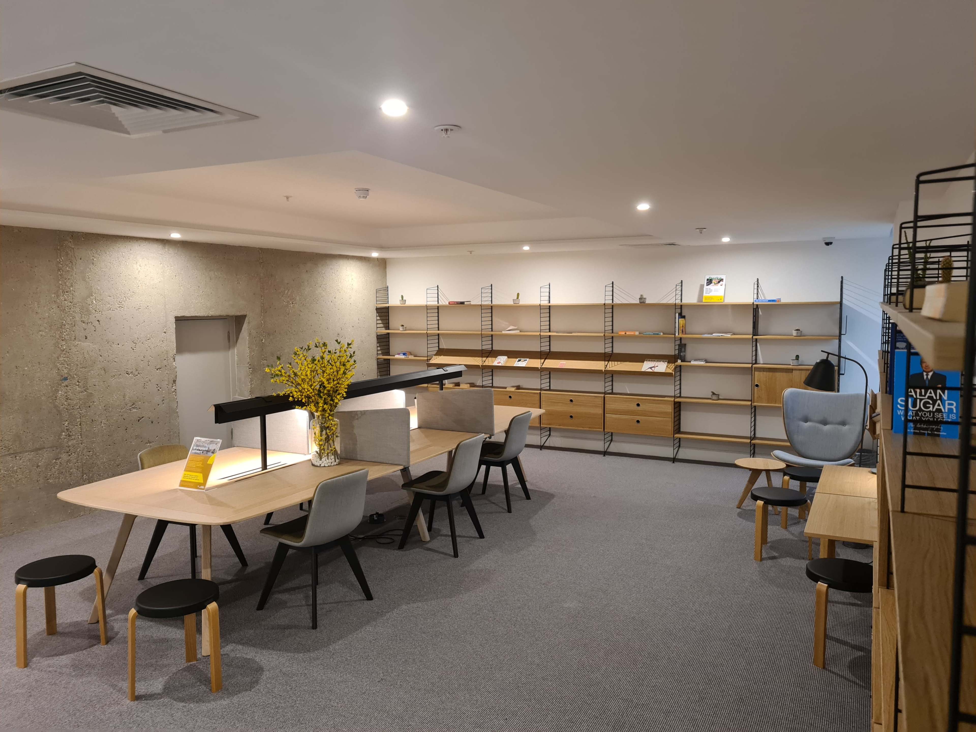 A modern office space with wooden tables, gray chairs, and shelves lined against the walls.