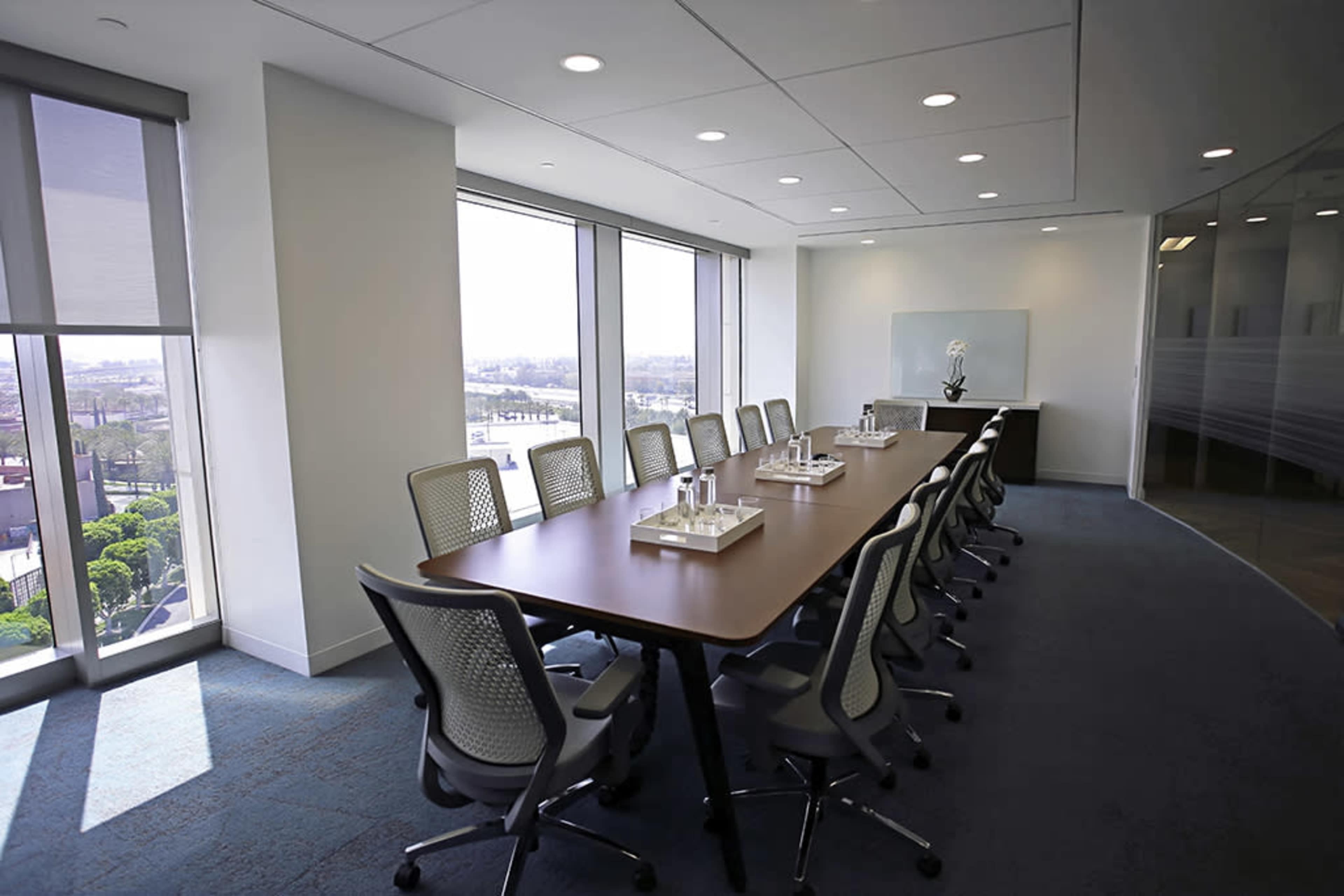 A modern conference room features a long table with chairs, large windows providing natural light, and a minimalist decor.