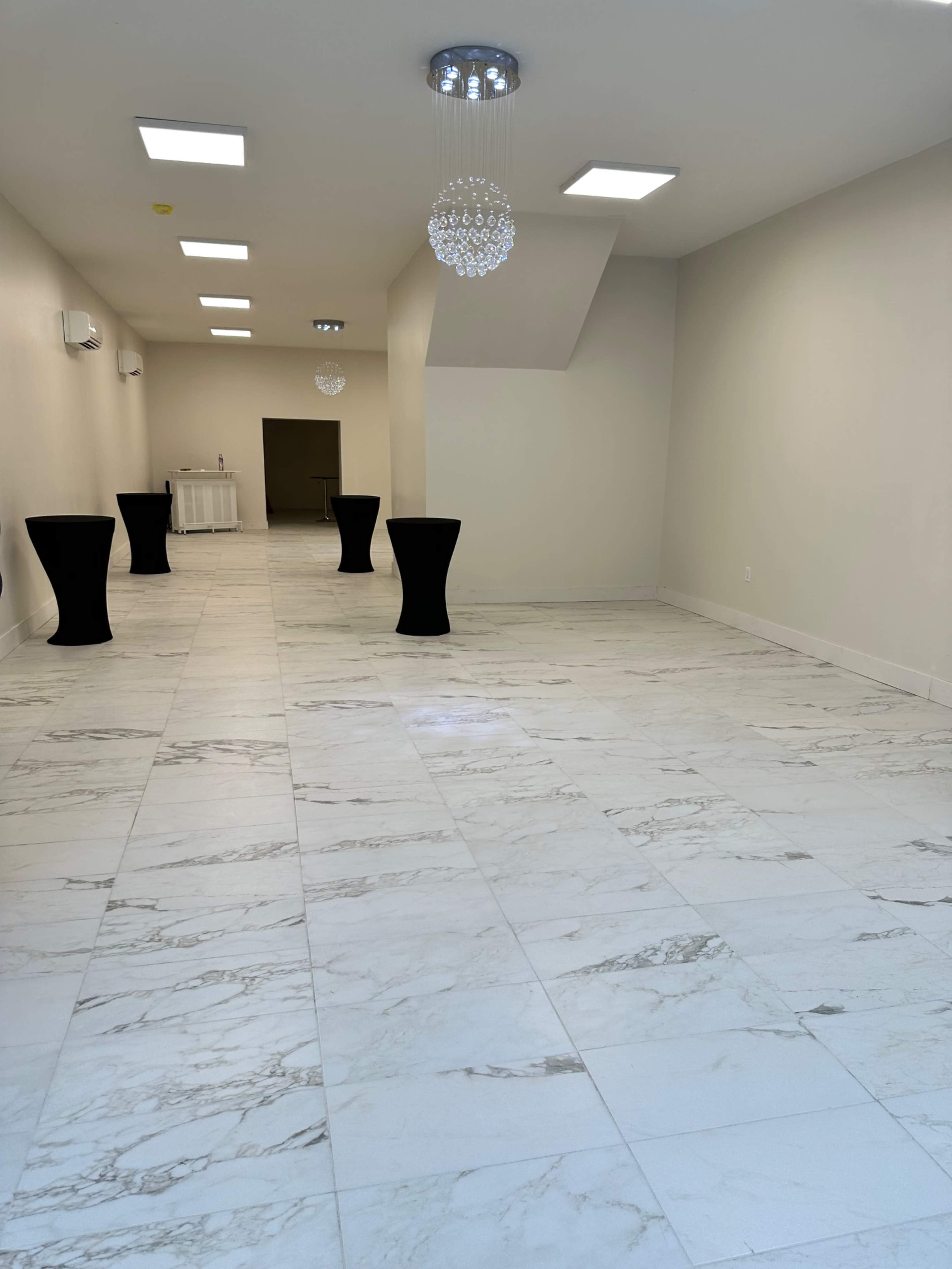 A spacious, empty room with marble flooring, tall ceiling, and modern lighting fixtures.