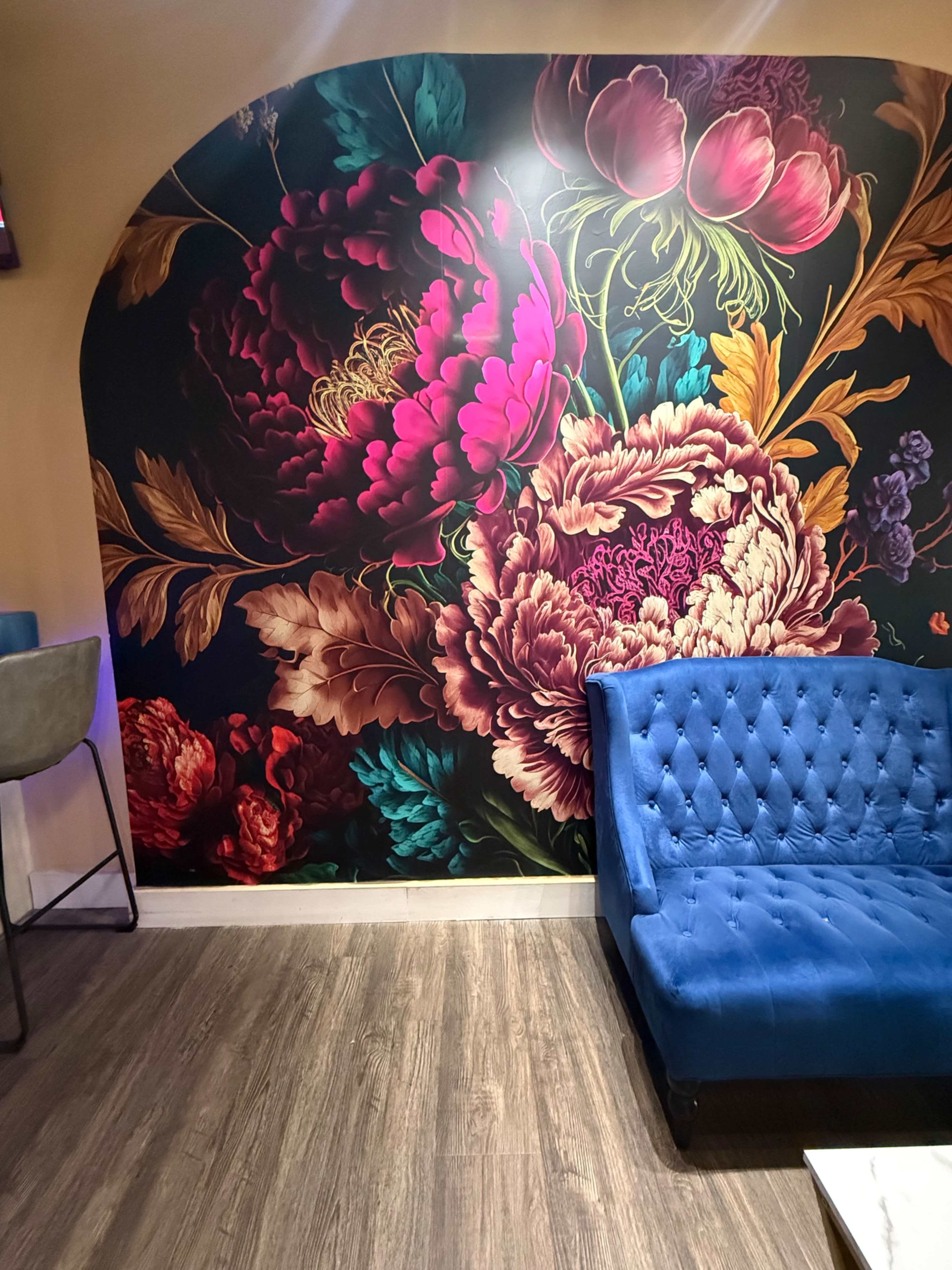 The image features a vibrant floral mural on the wall behind a blue tufted sofa in a cozy indoor space.