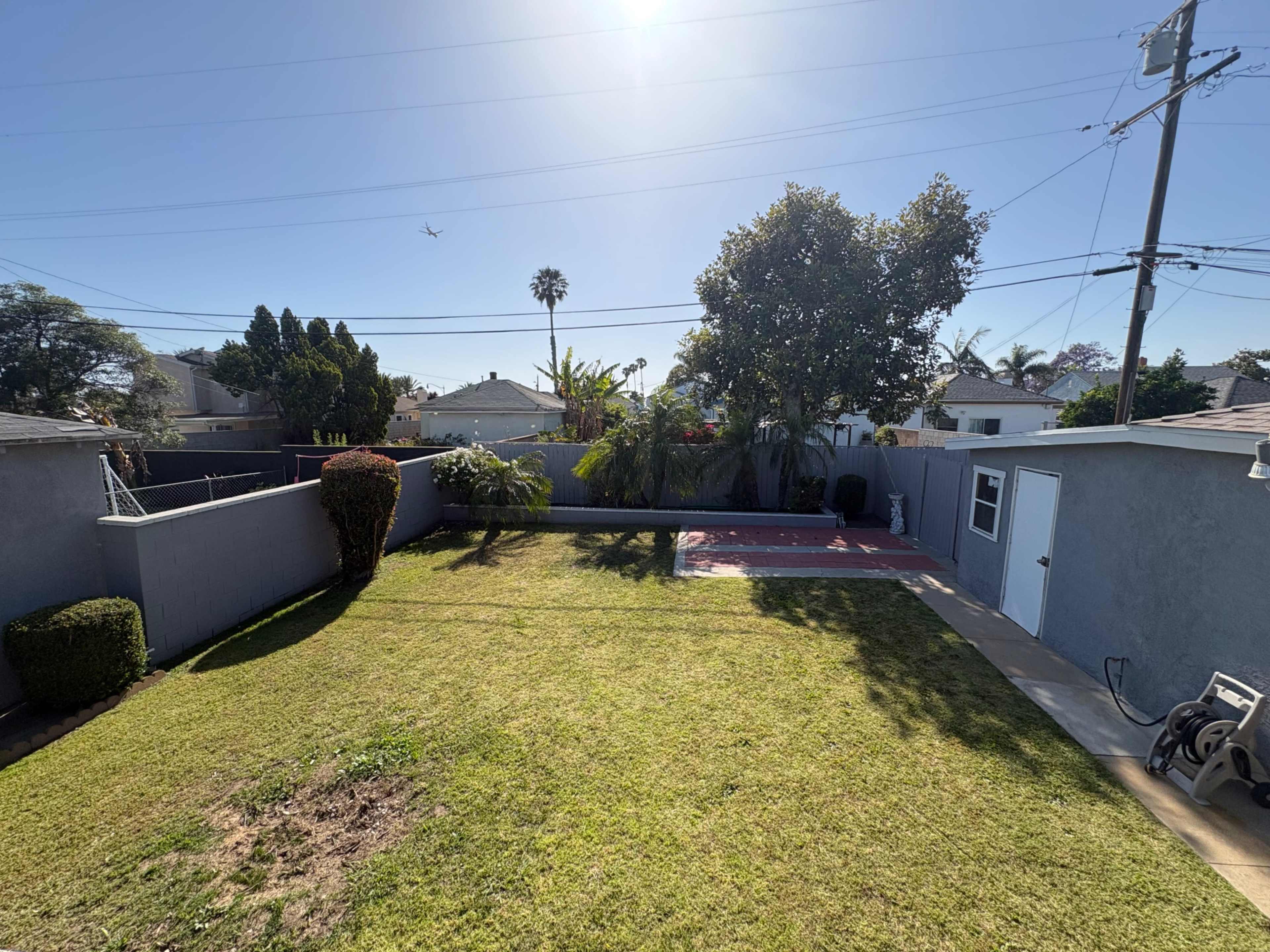 The image shows a sunny backyard with a grassy area, a patio, and a small shed.