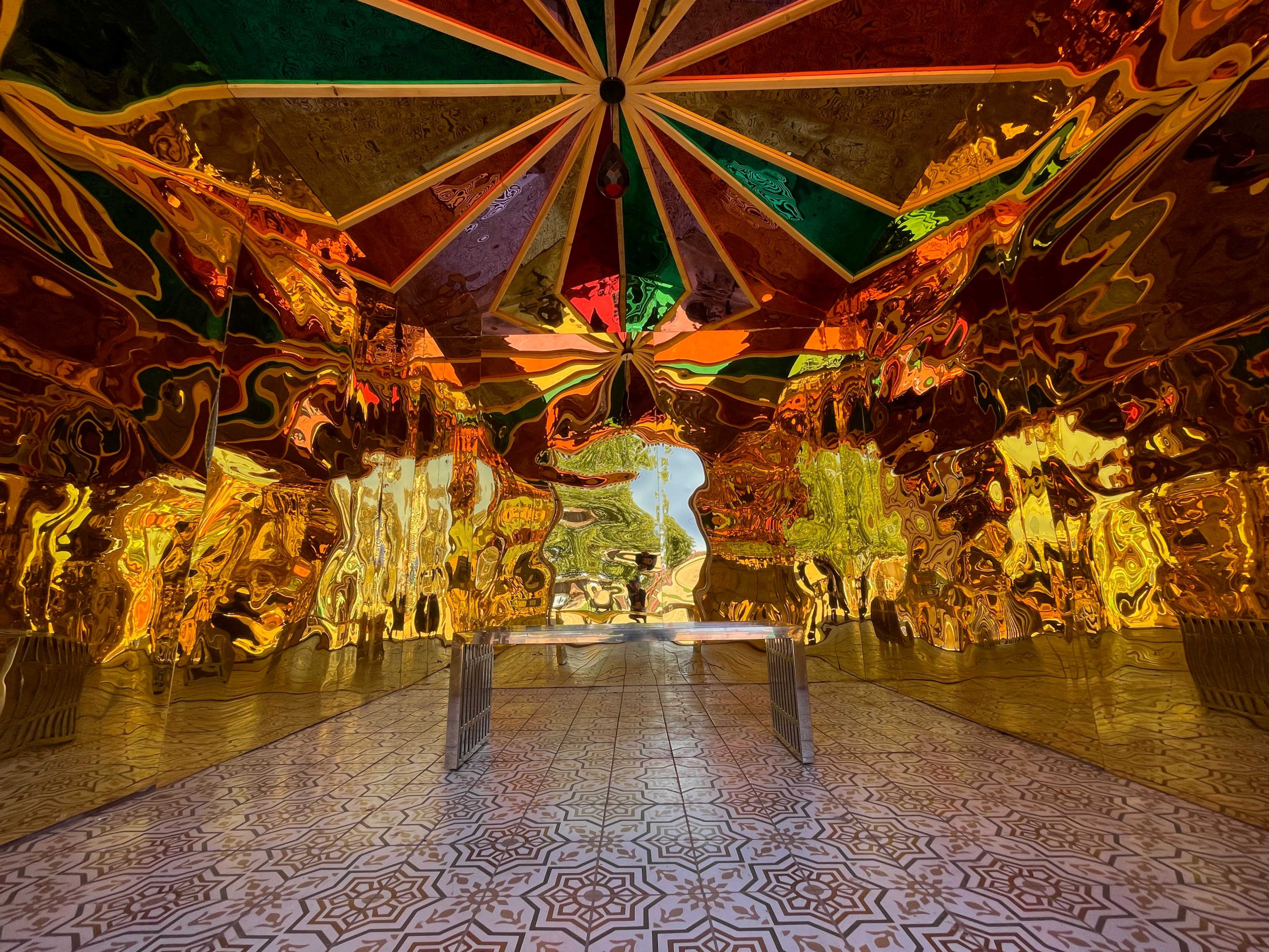 A reflective, metallic interior space with a colorful striped ceiling and a patterned tiled floor.