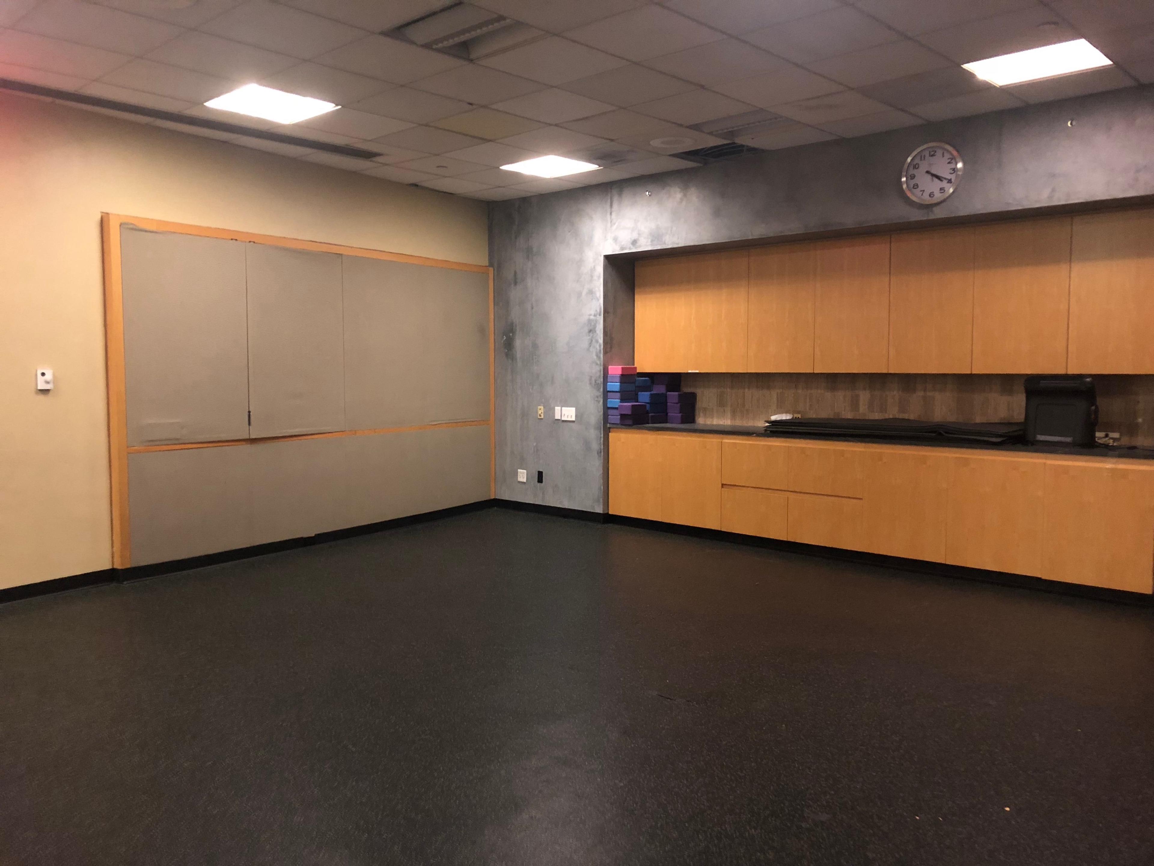 An empty room with a dark floor, a wall-mounted clock, and cabinets along one side.