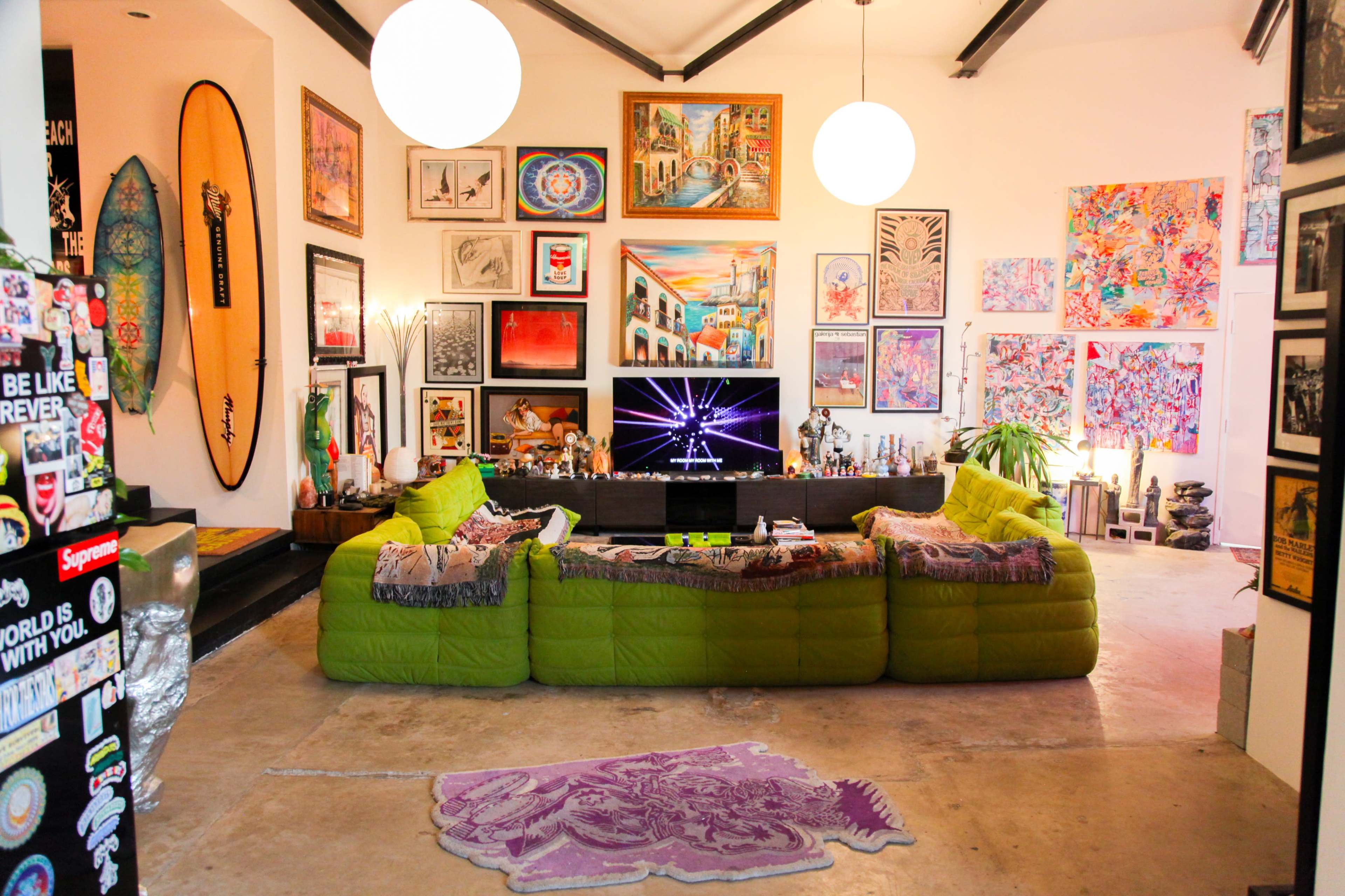 A vibrant living room features a large green sectional sofa, an array of colorful wall art, a modern entertainment center, and various decorative elements throughout the space.