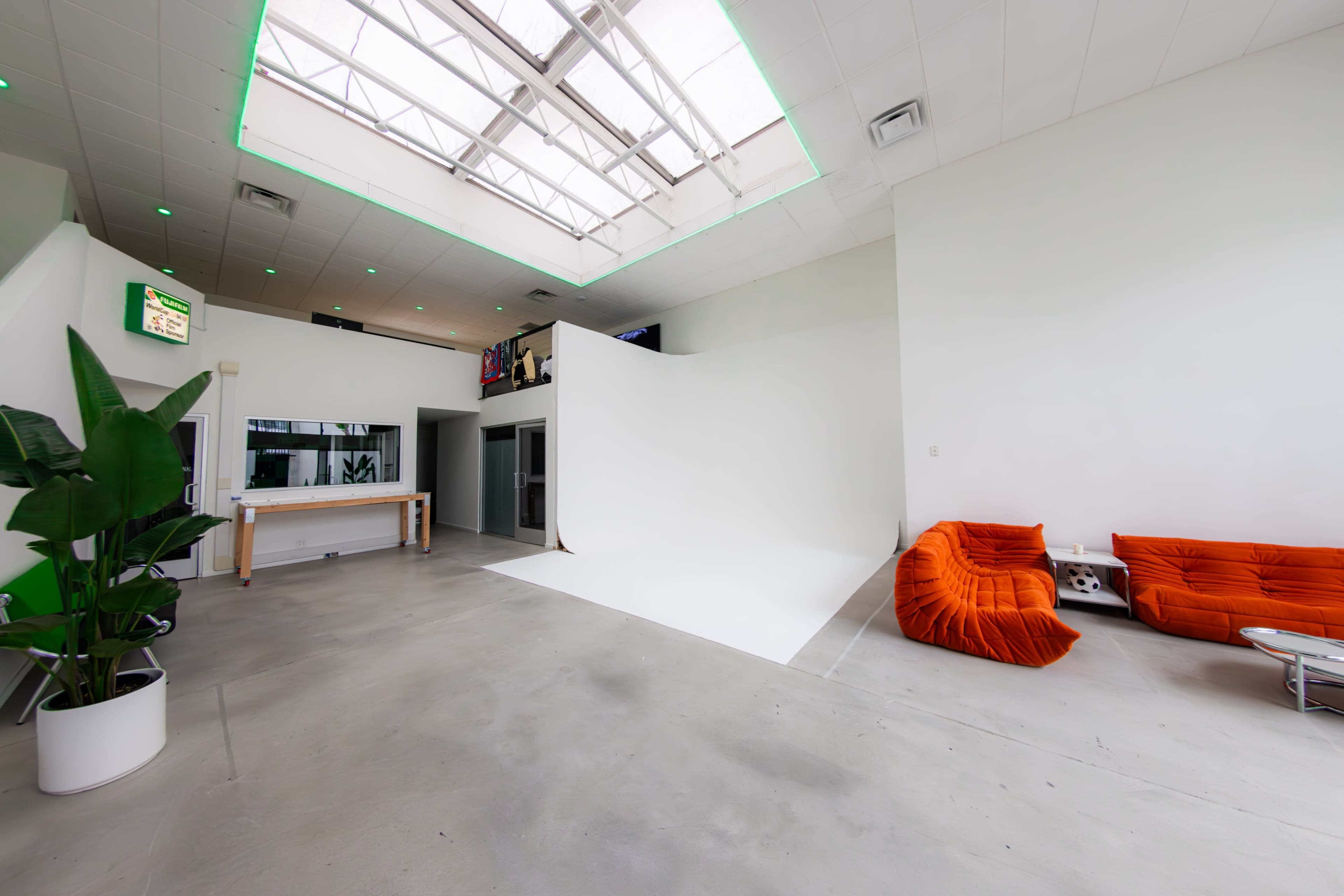 A spacious interior with a white backdrop, an orange seating area, large skylights, and a plant in a pot.