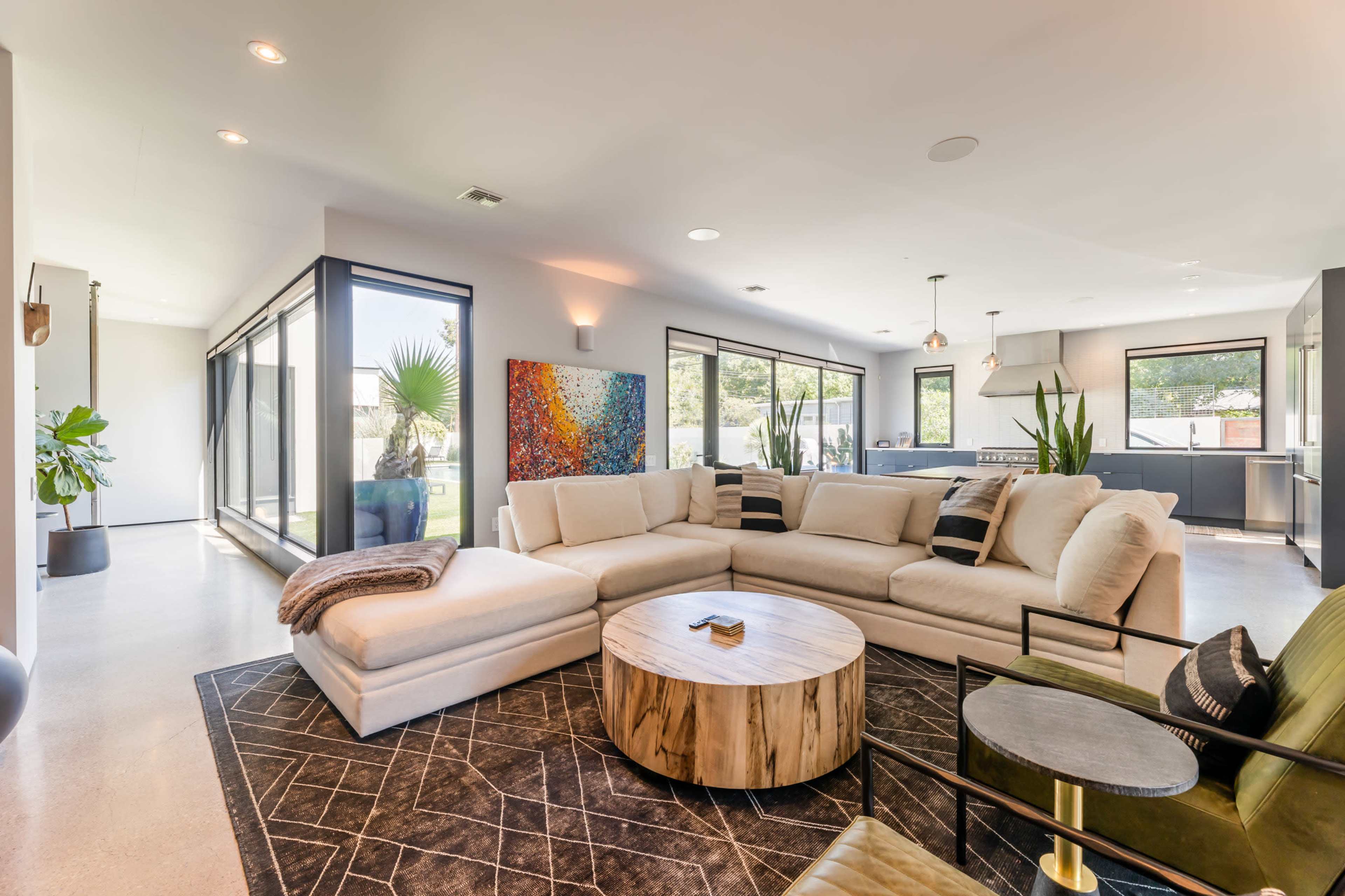 A modern living room with a large sectional sofa, a circular wooden coffee table, and large windows providing a view of the outdoors.