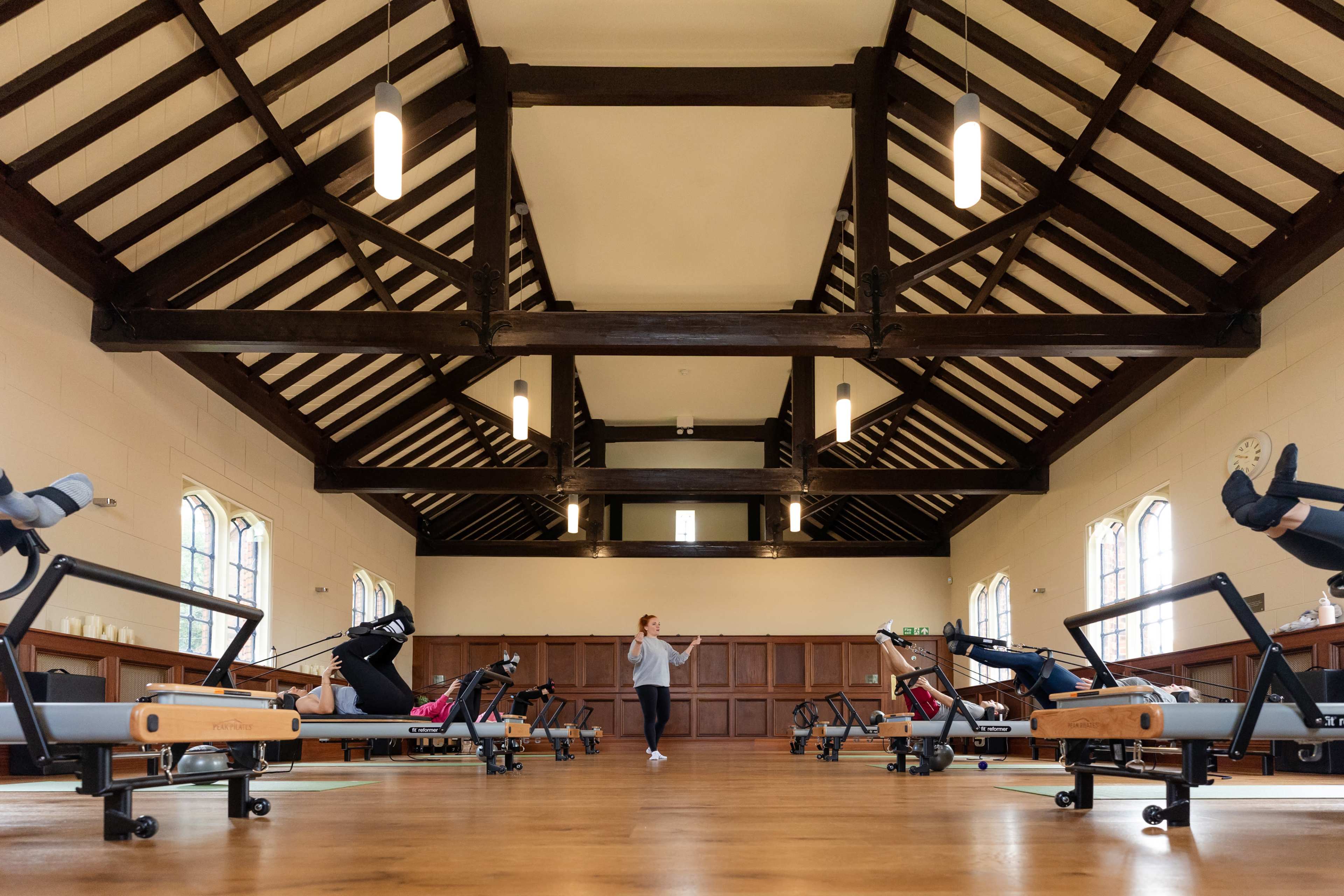 A spacious fitness studio features several reformer machines arranged in rows beneath a high, beamed ceiling.