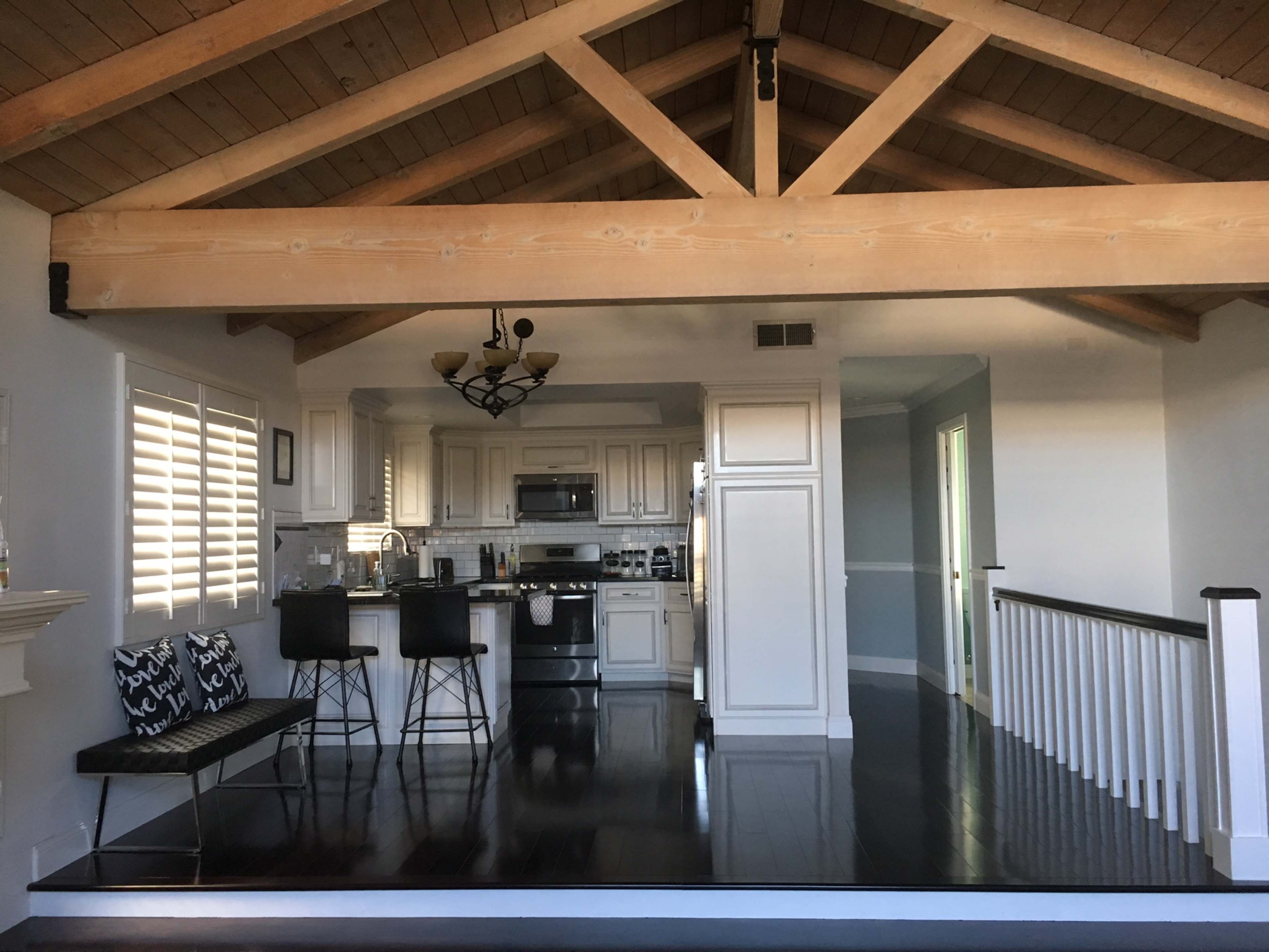 A spacious living area with a kitchen in the background, featuring a high wooden beam ceiling and sleek black flooring.