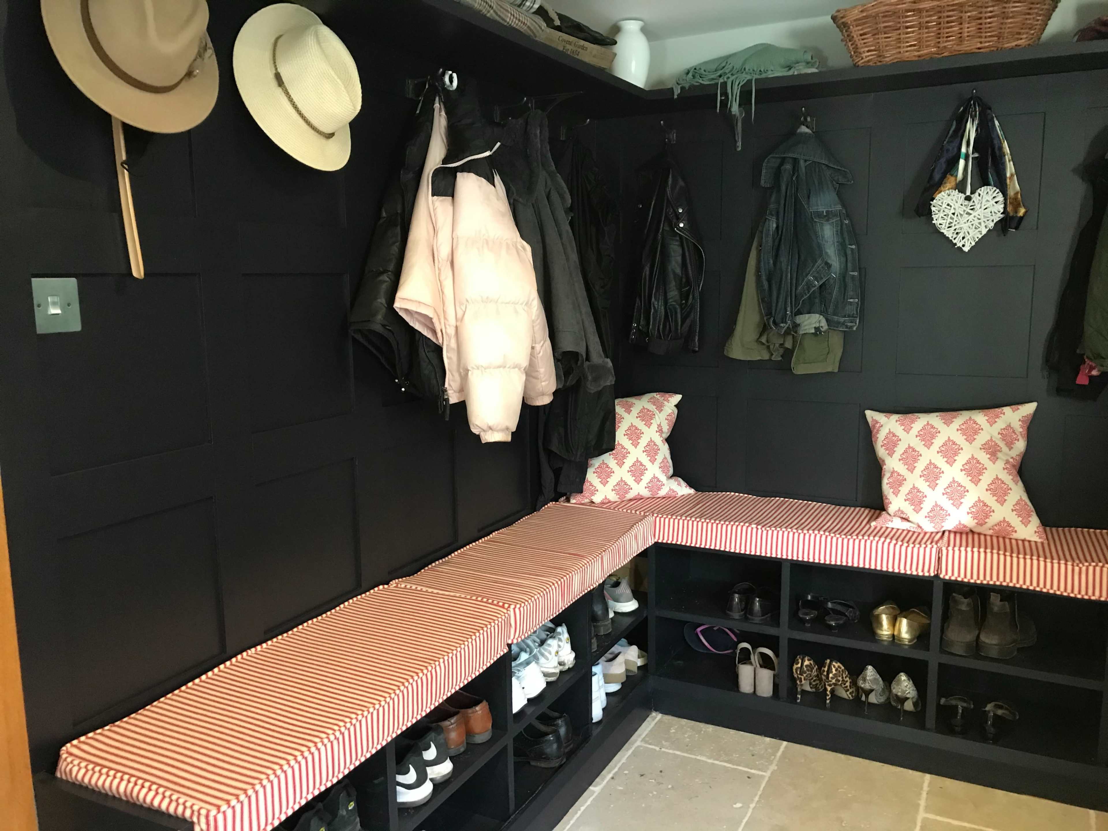 A mudroom features black paneled walls, seating with striped cushions, and organized storage for hats, jackets, and shoes.