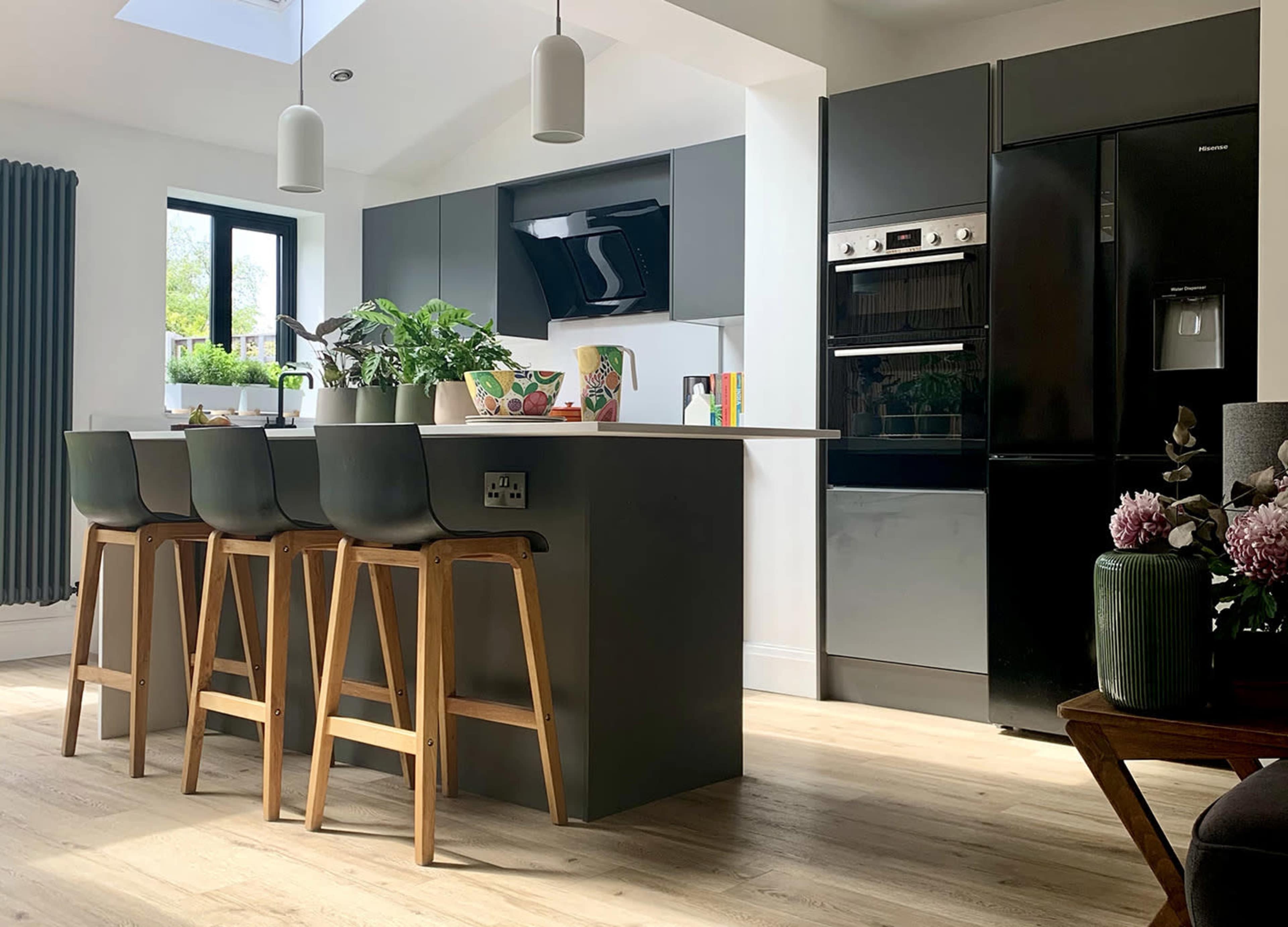 A modern kitchen features dark cabinetry, a dining area with wooden stools, and large windows allowing natural light.