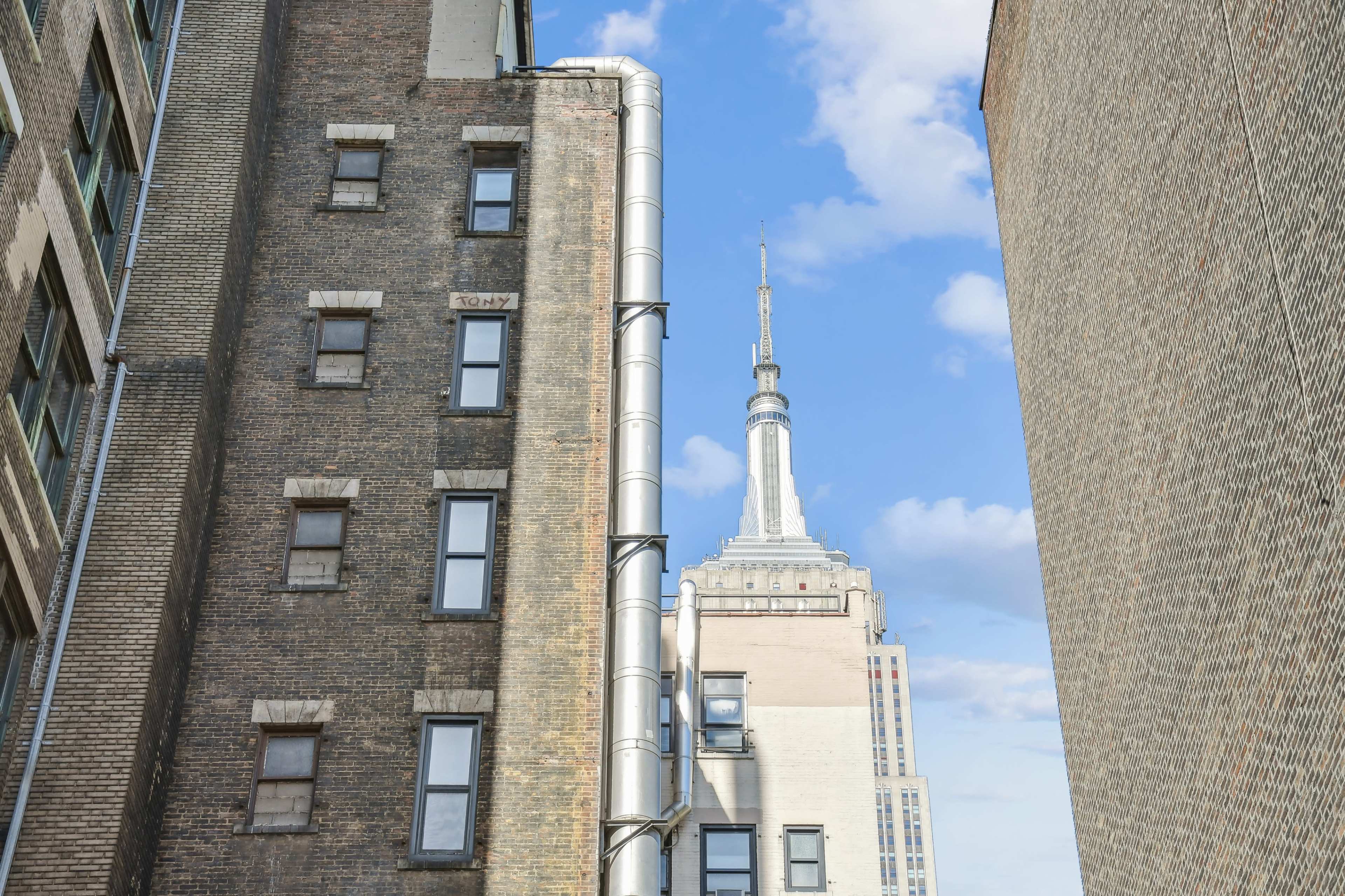 The image shows a view between two buildings, featuring the Empire State Building prominently against a blue sky.