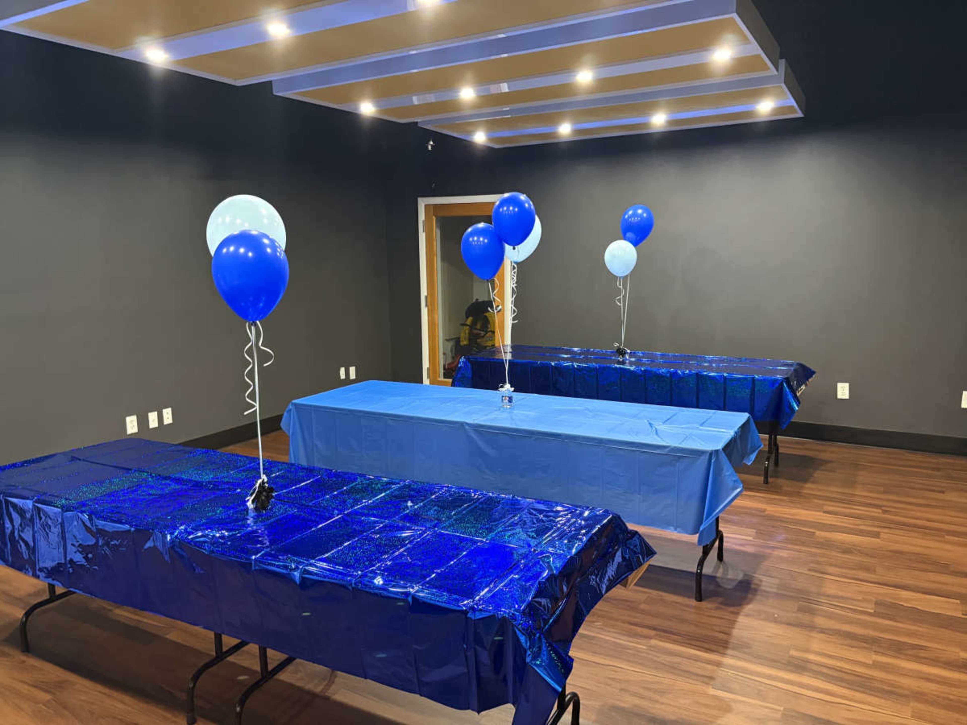 The image shows a room with four blue-covered tables, each adorned with blue and light blue balloons.