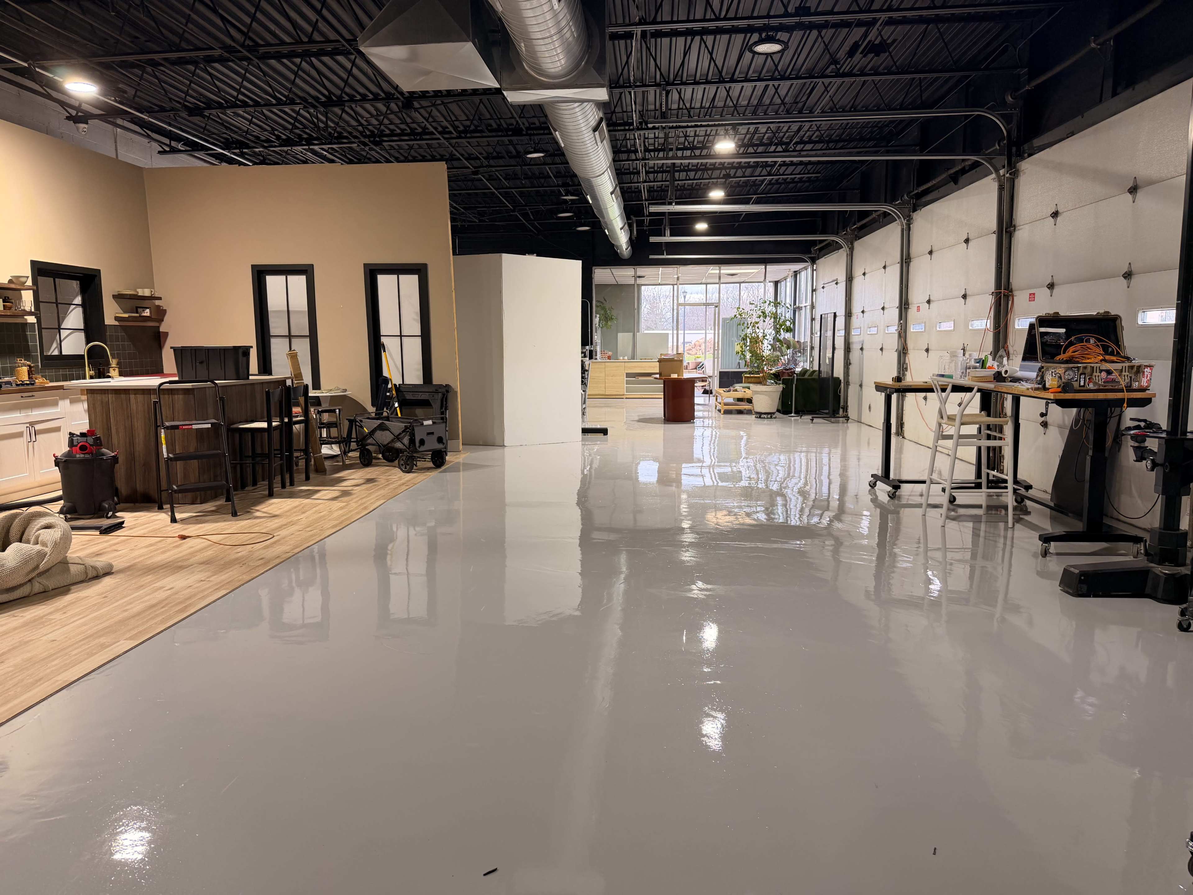 The image shows a spacious interior with polished gray floors, featuring a kitchen area, several workstations, and areas furnished for different activities.