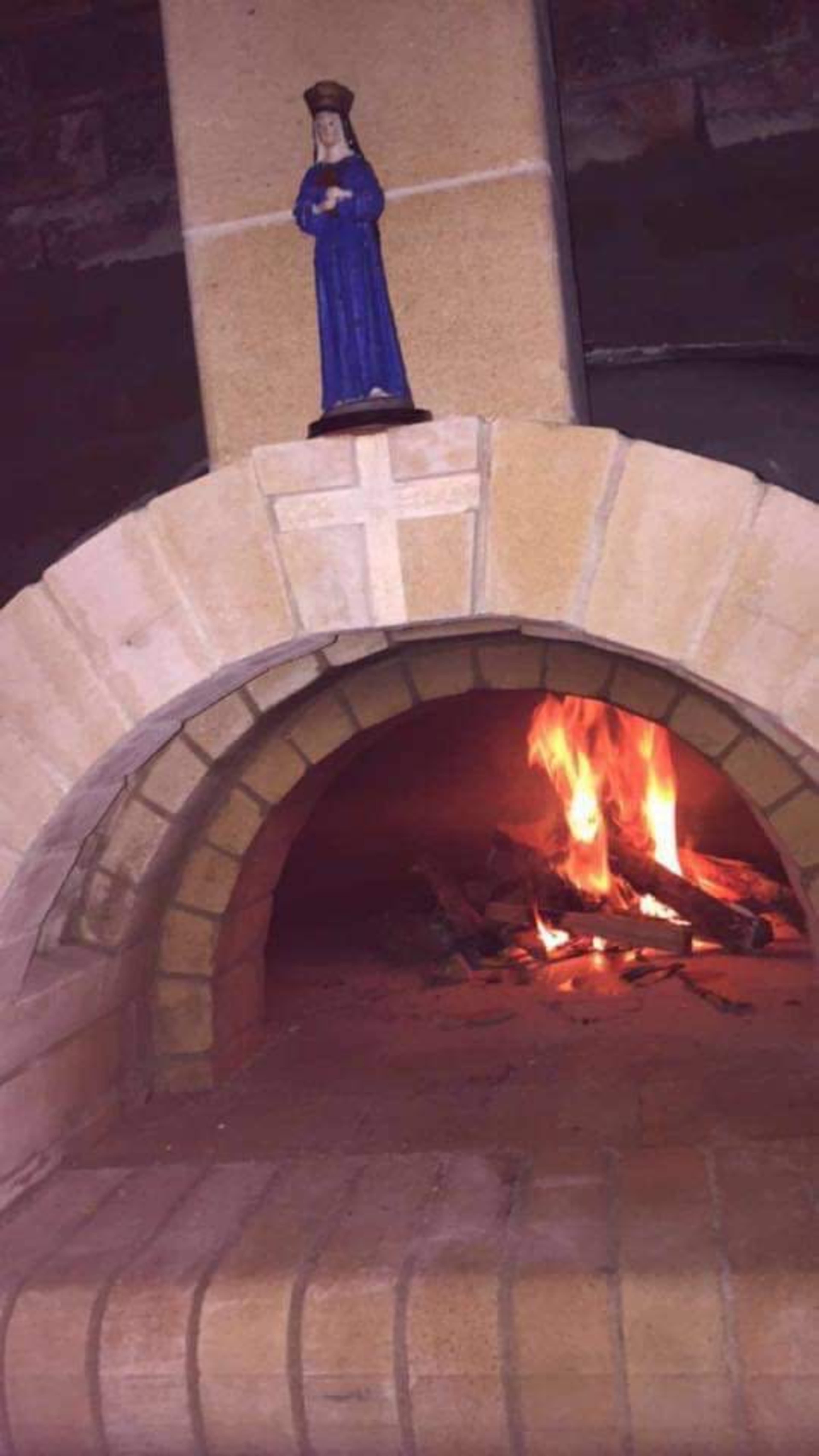 A brick fireplace with a figurine of a woman on top and a fire burning inside.