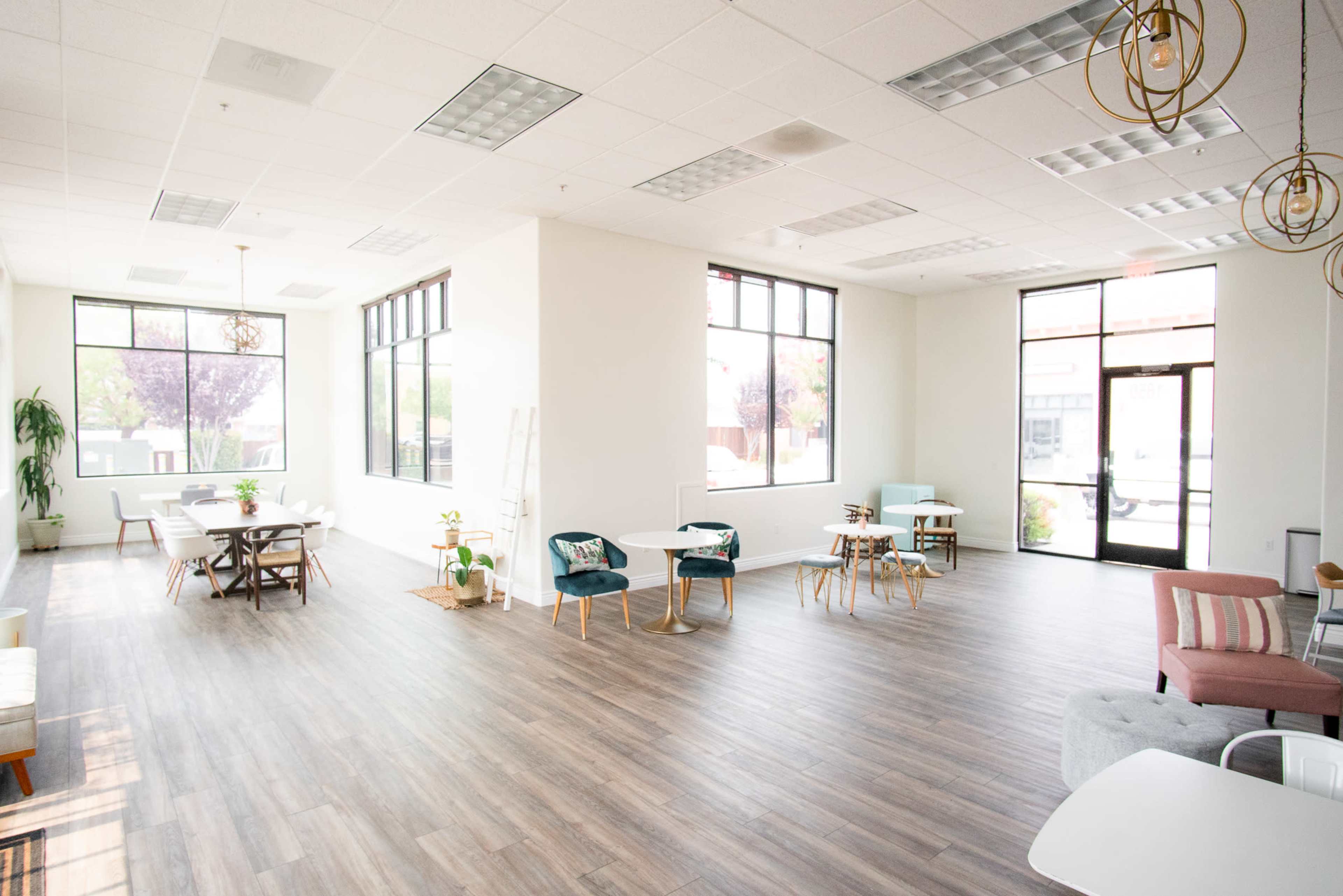 A spacious, modern interior with large windows, wooden flooring, and various seating arrangements including tables and chairs.