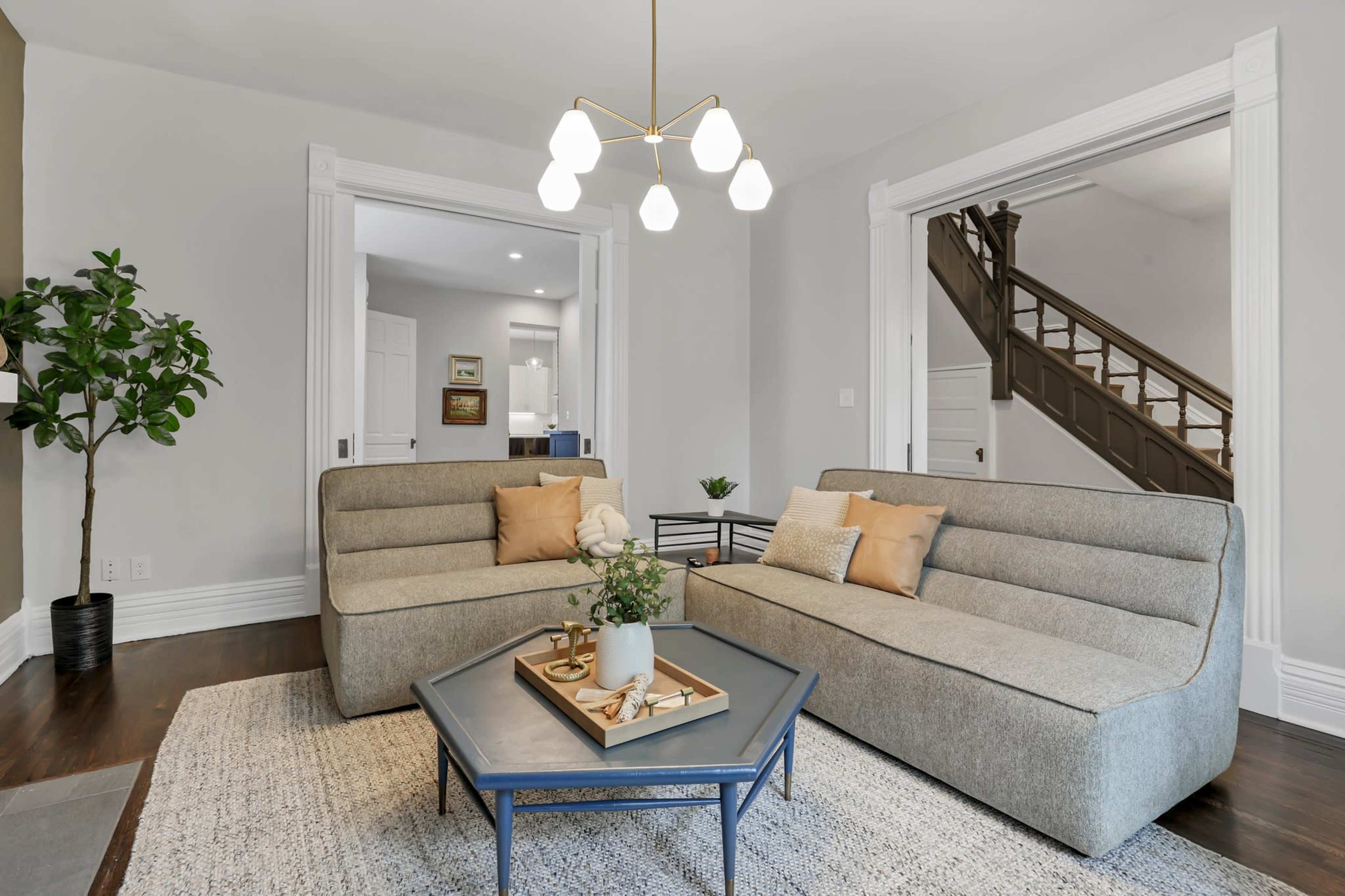A spacious living room features two modern sofas flanking a coffee table, with a view of a staircase and other rooms through open doorways.