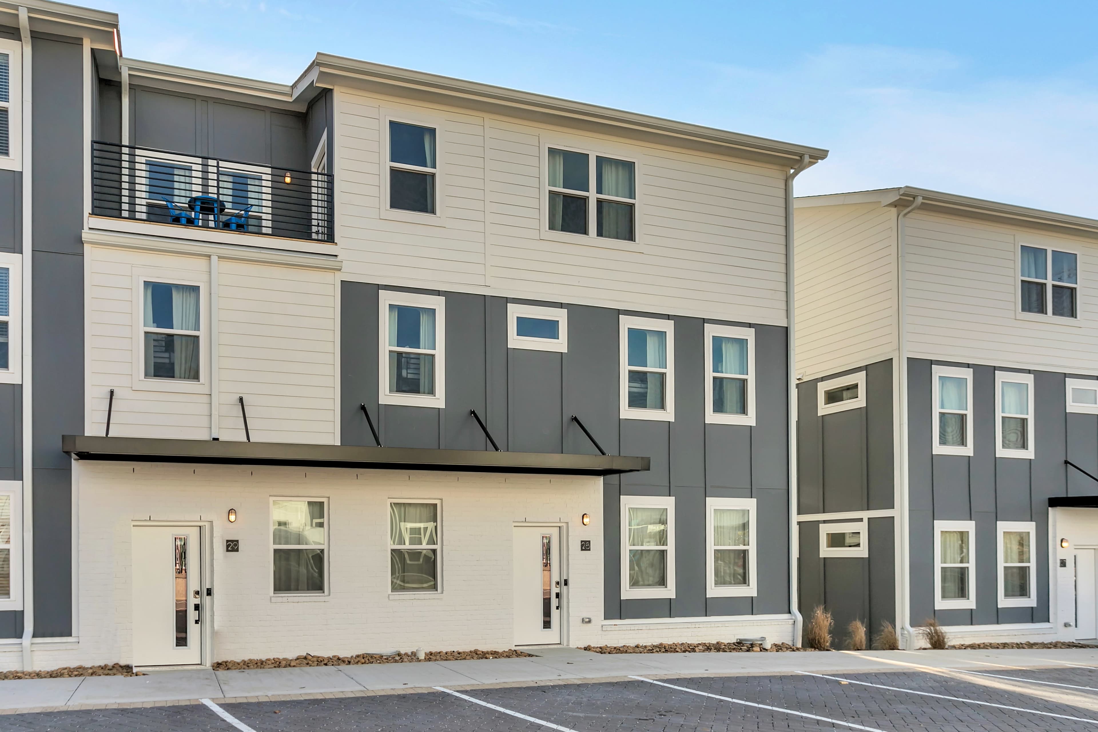 A modern, two-story apartment building with a mix of white and gray exterior panels and several parking spaces in front.