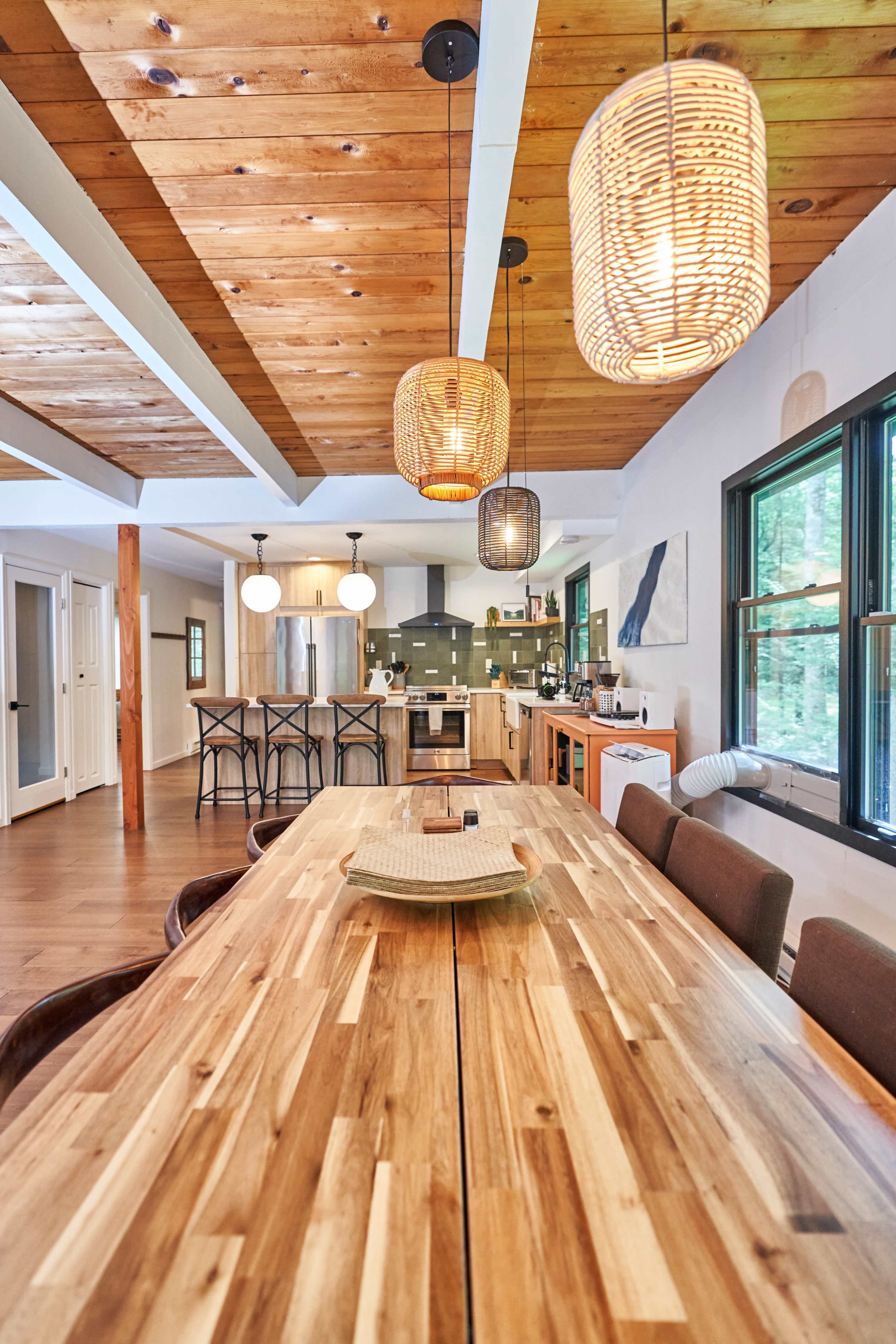 The image shows a modern dining area featuring a wooden table with eight chairs, pendant lighting, and an open kitchen in the background.