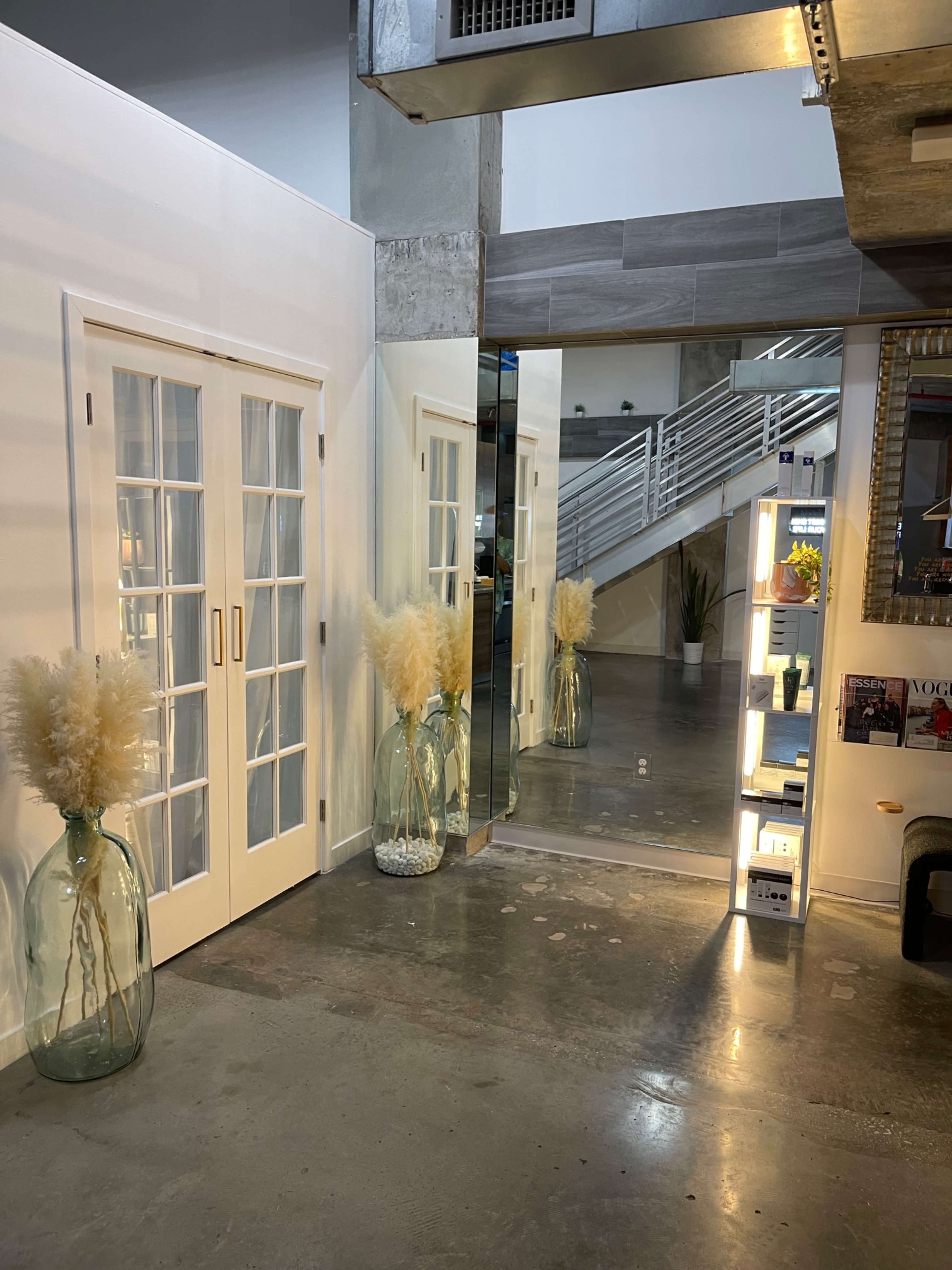 The image shows a well-lit interior space featuring a pair of glass doors, a large mirror, and decorative elements including a tall vase with dried vegetation.