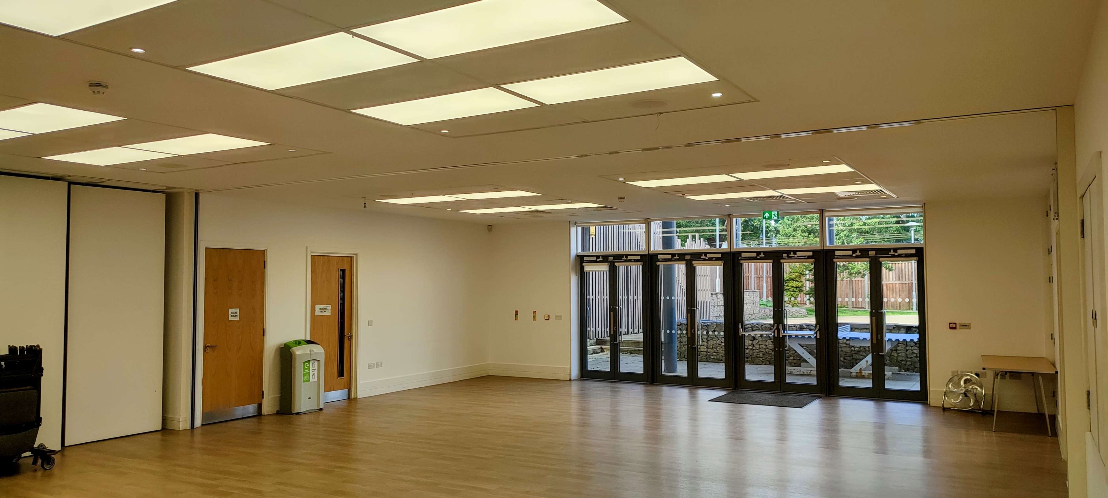 A spacious, empty room with large windows and several light panels on the ceiling.