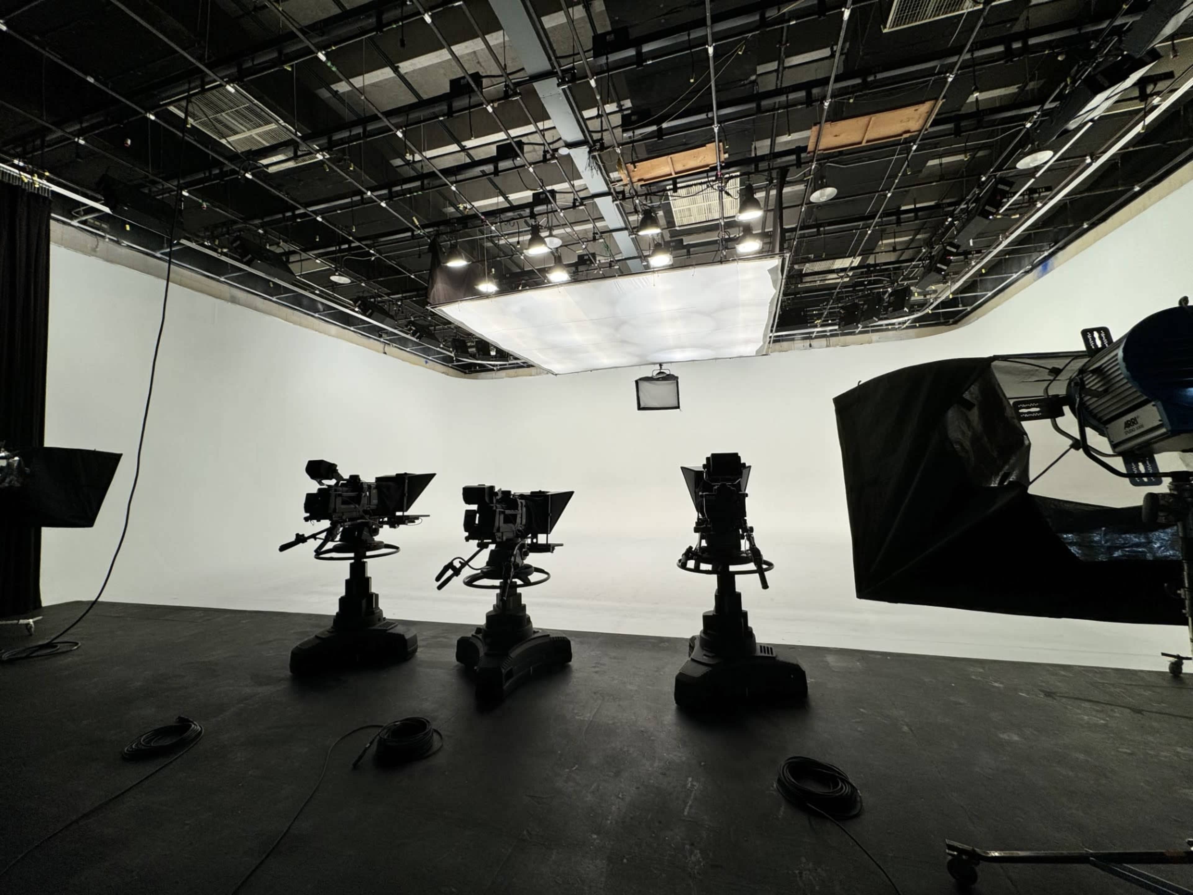 A television studio with three camera setups facing a blank white backdrop.