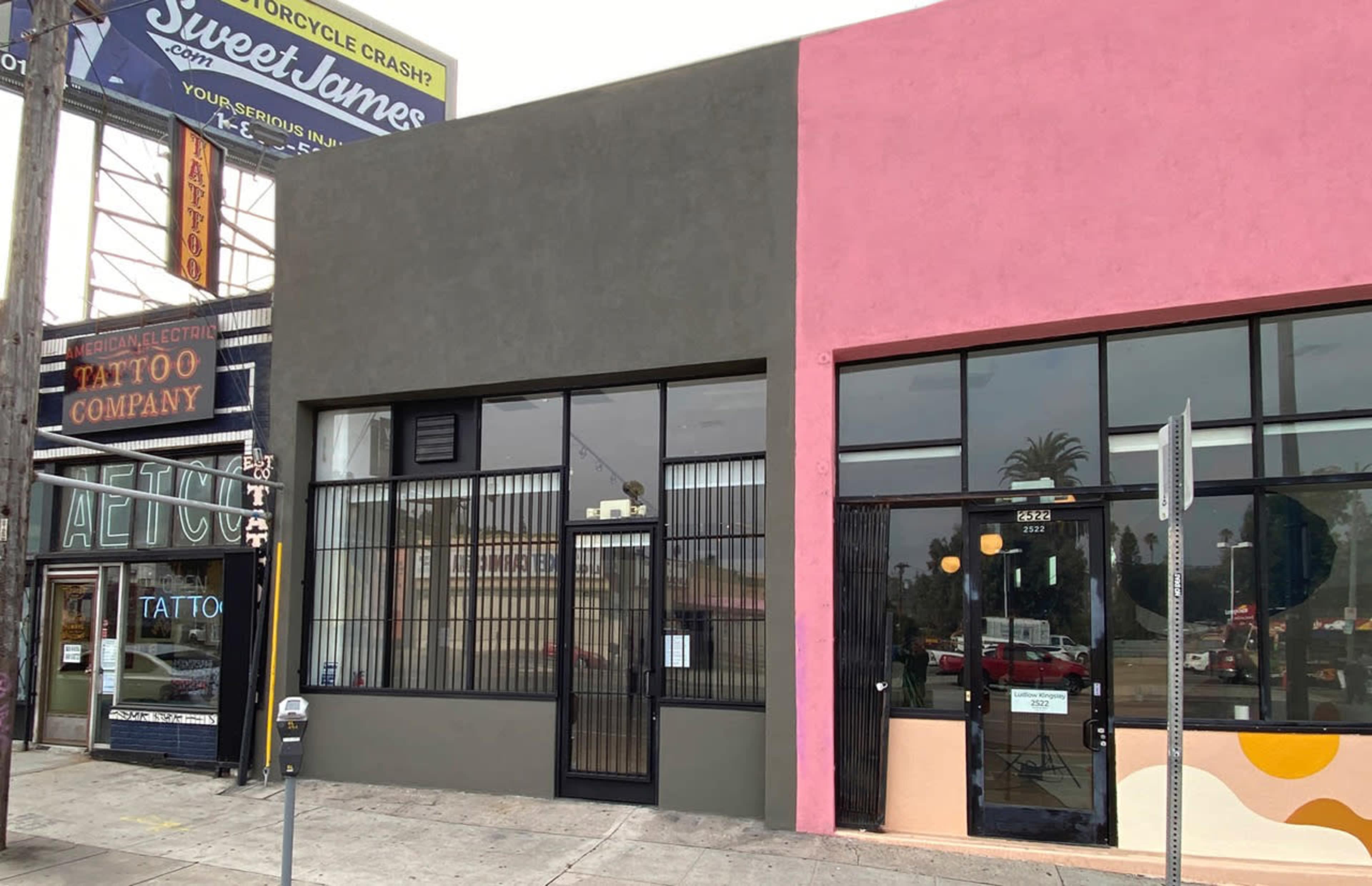 The image shows two adjacent storefronts, one with a gray exterior and another with a pink facade, along a city street.