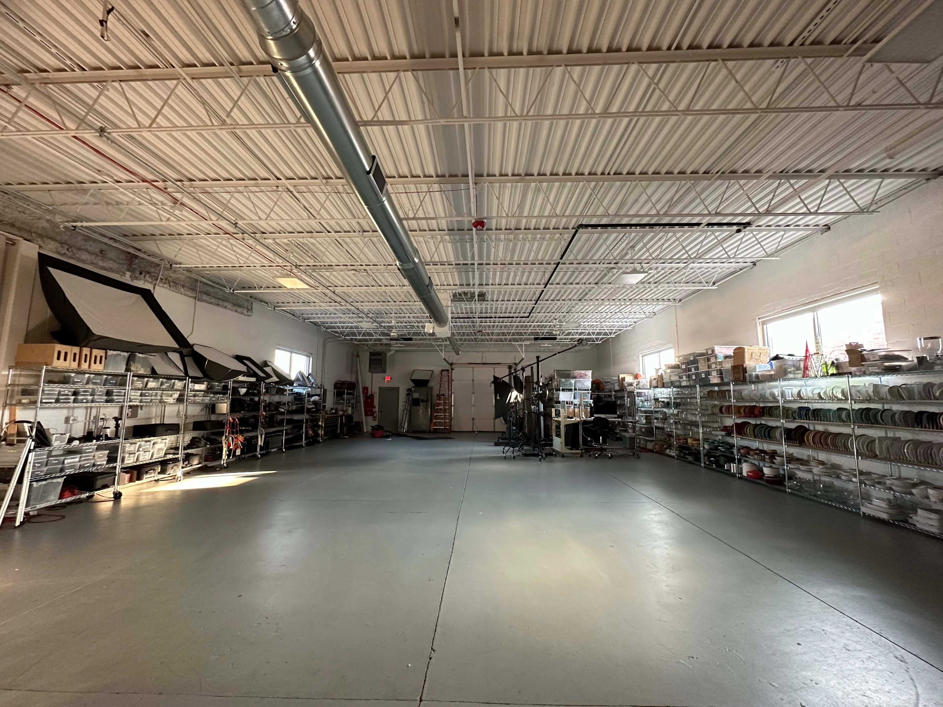 A spacious warehouse interior with shelving units filled with various items along the walls and a clear, empty floor area.