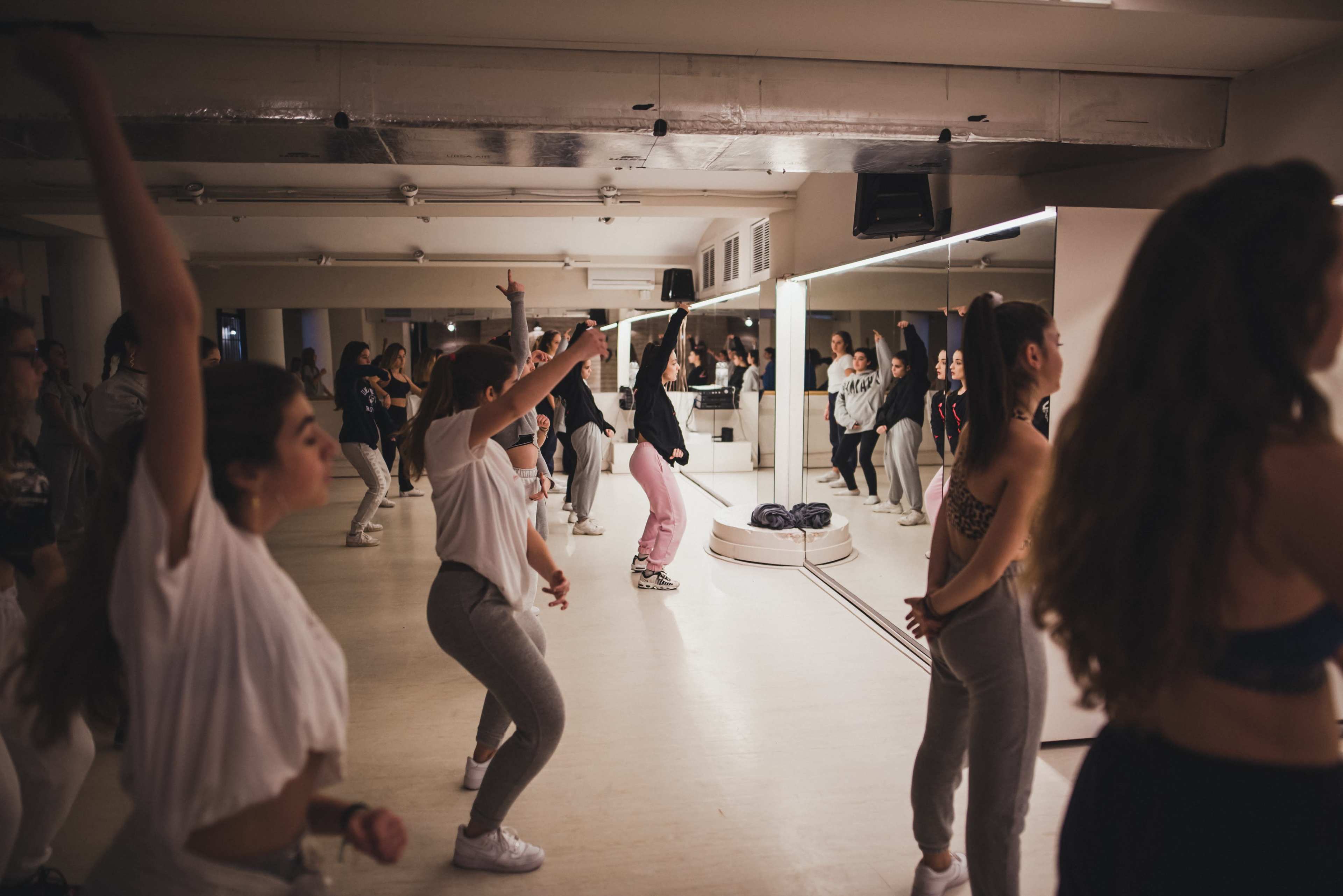 A group of dancers practice choreography in a mirrored studio.