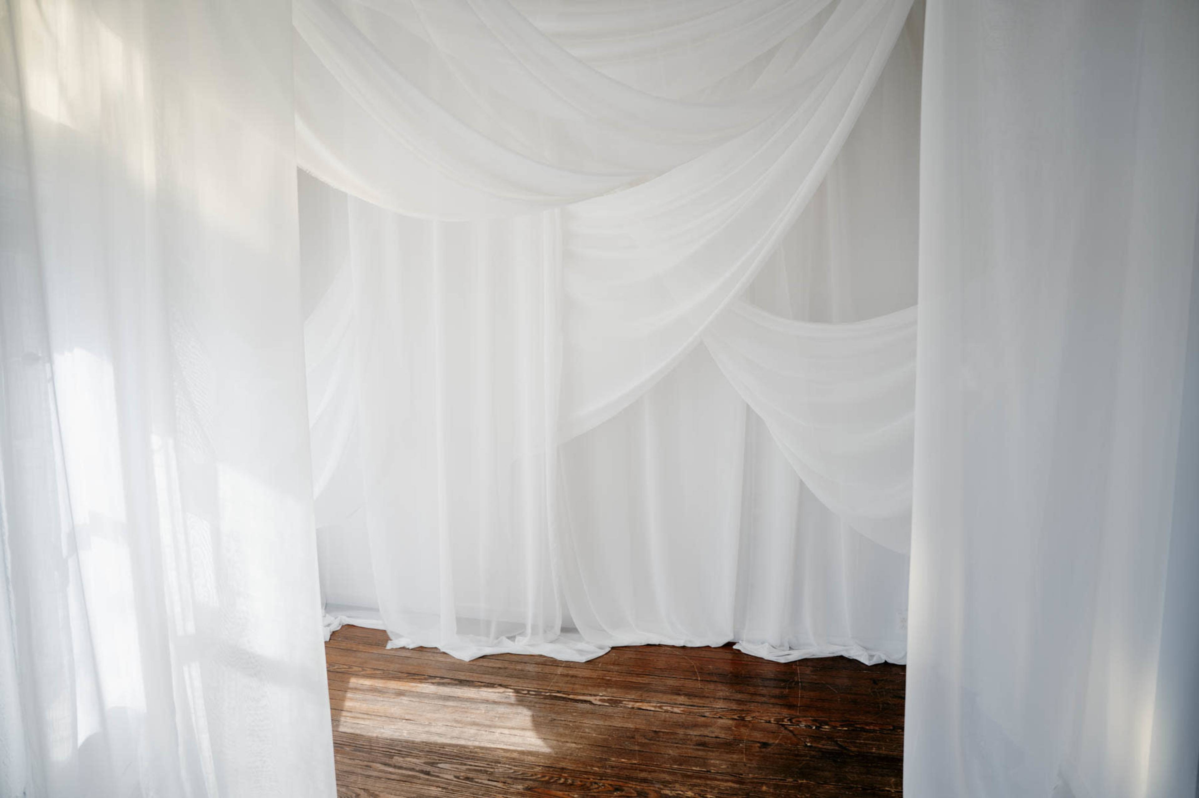 The image shows a softly draped white fabric backdrop in a room with wooden floors.