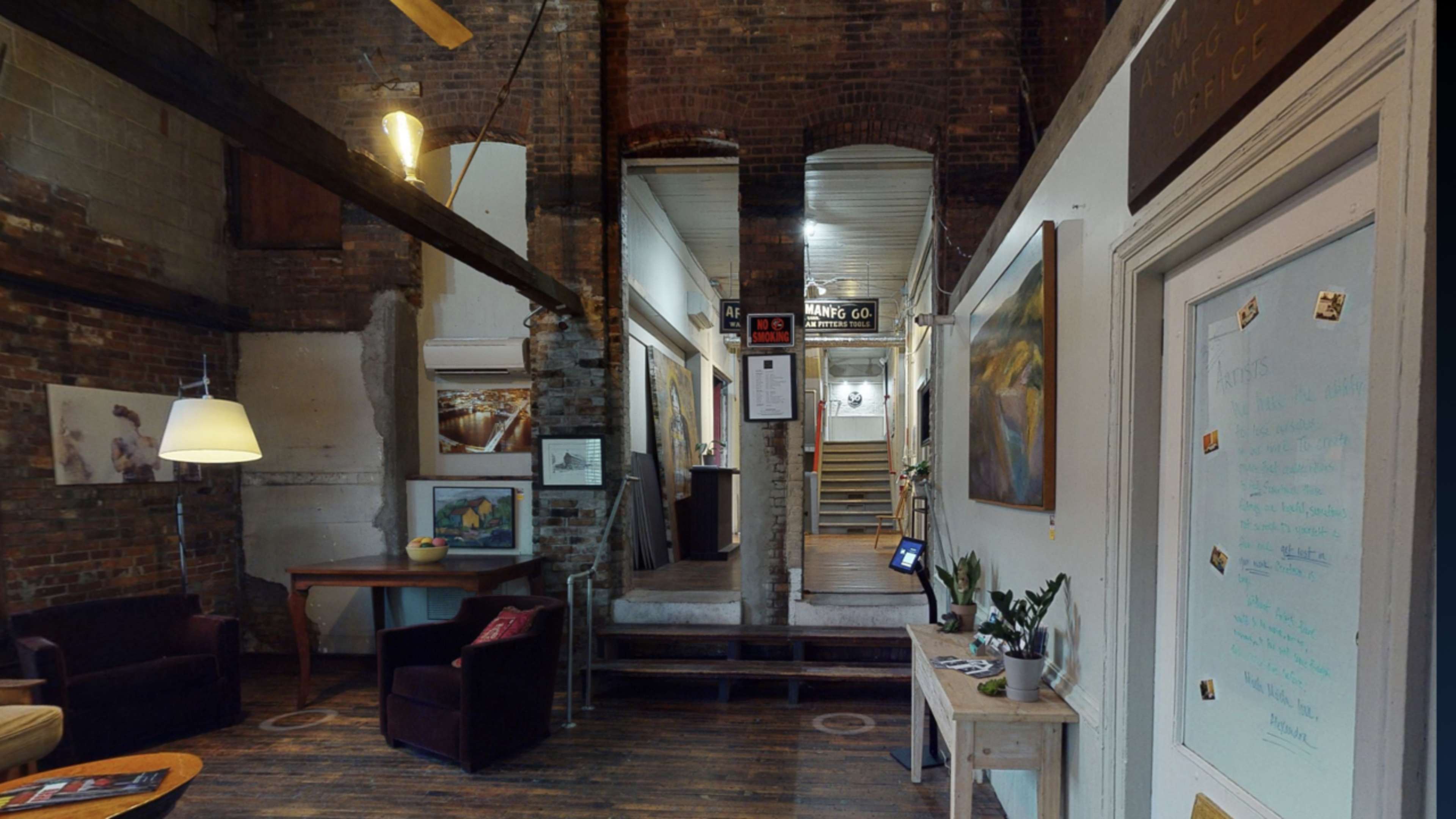 A rustic interior hallway featuring exposed brick walls, wooden beams, and various artworks displayed on the walls.