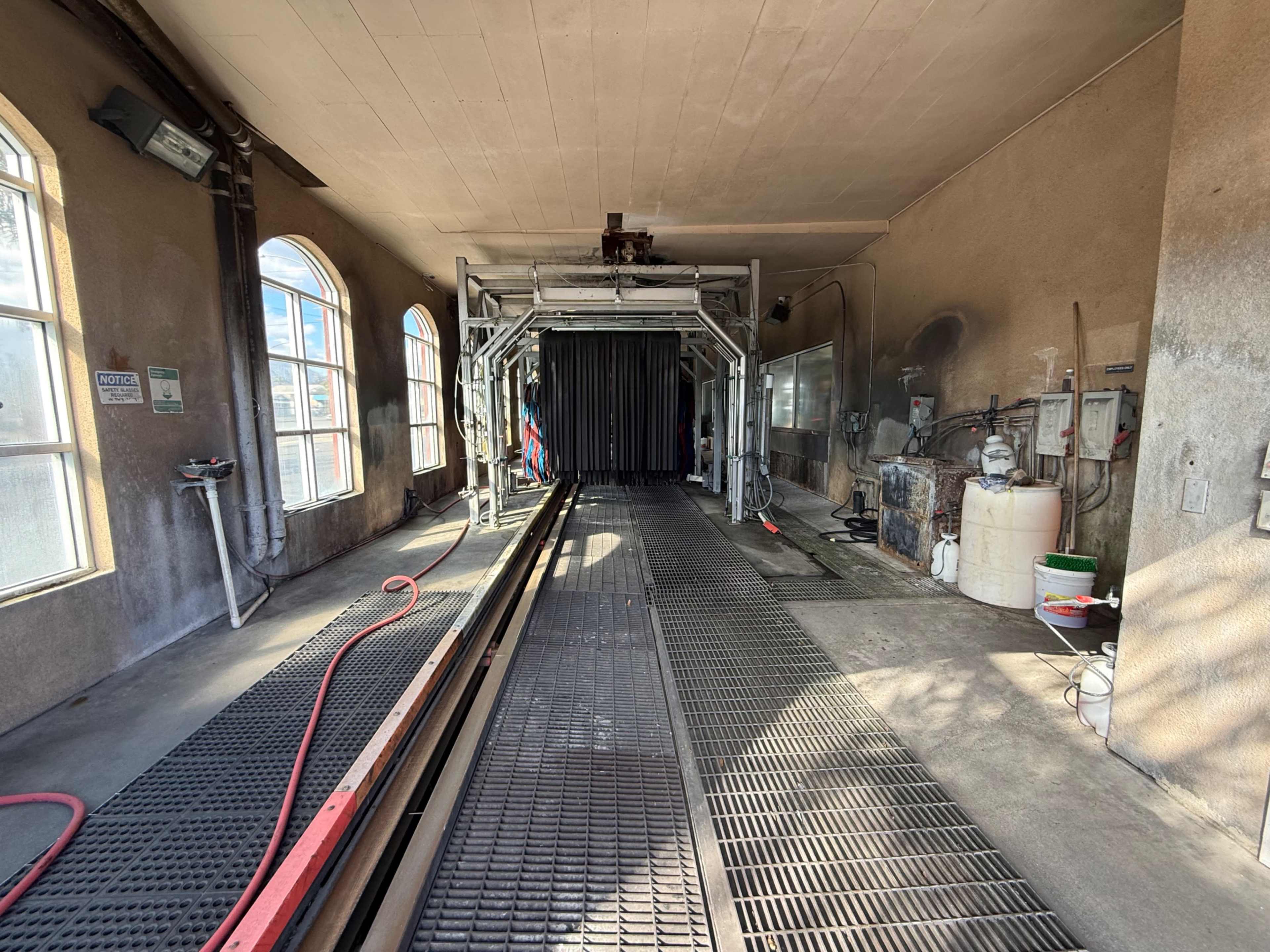 The image shows the interior of a car wash facility with tracks leading to a dark entrance and various equipment and tools along the walls.