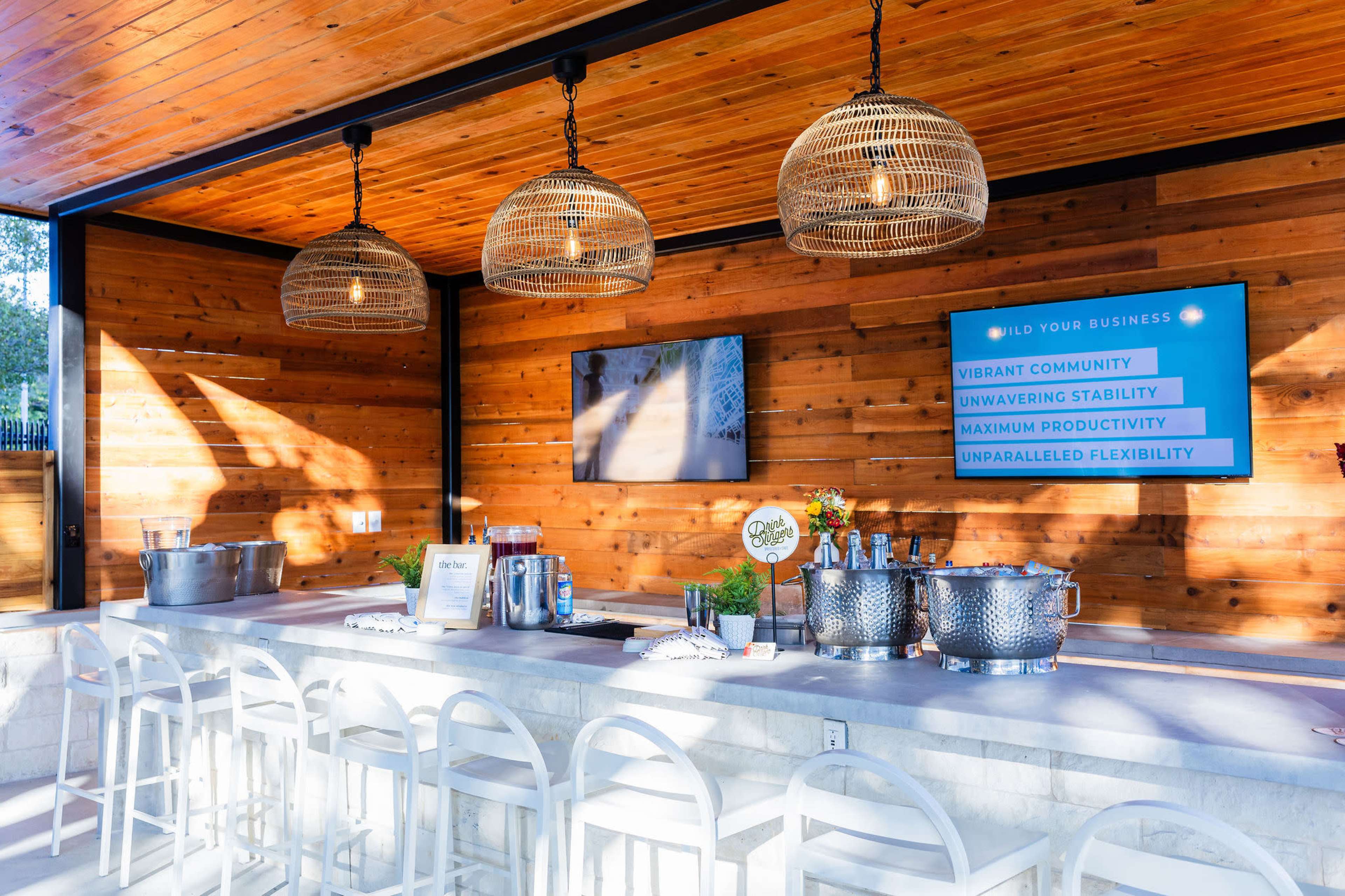A stylish bar area with hanging light fixtures, a marble counter, and a wooden wall, displaying promotional materials on a screen.
