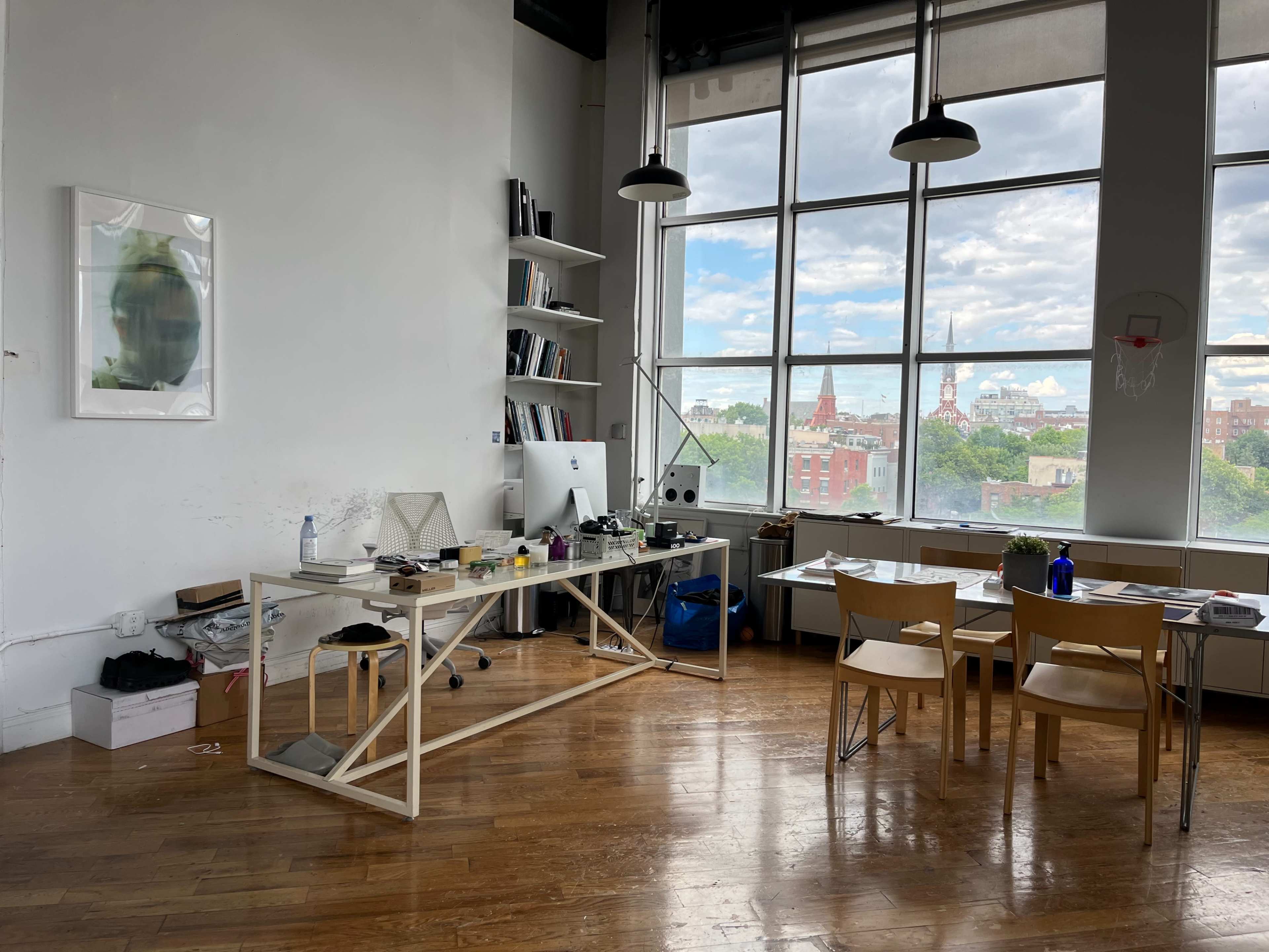 A spacious, bright office with a large window offering a view of a city skyline, featuring a minimalist desk and several chairs.