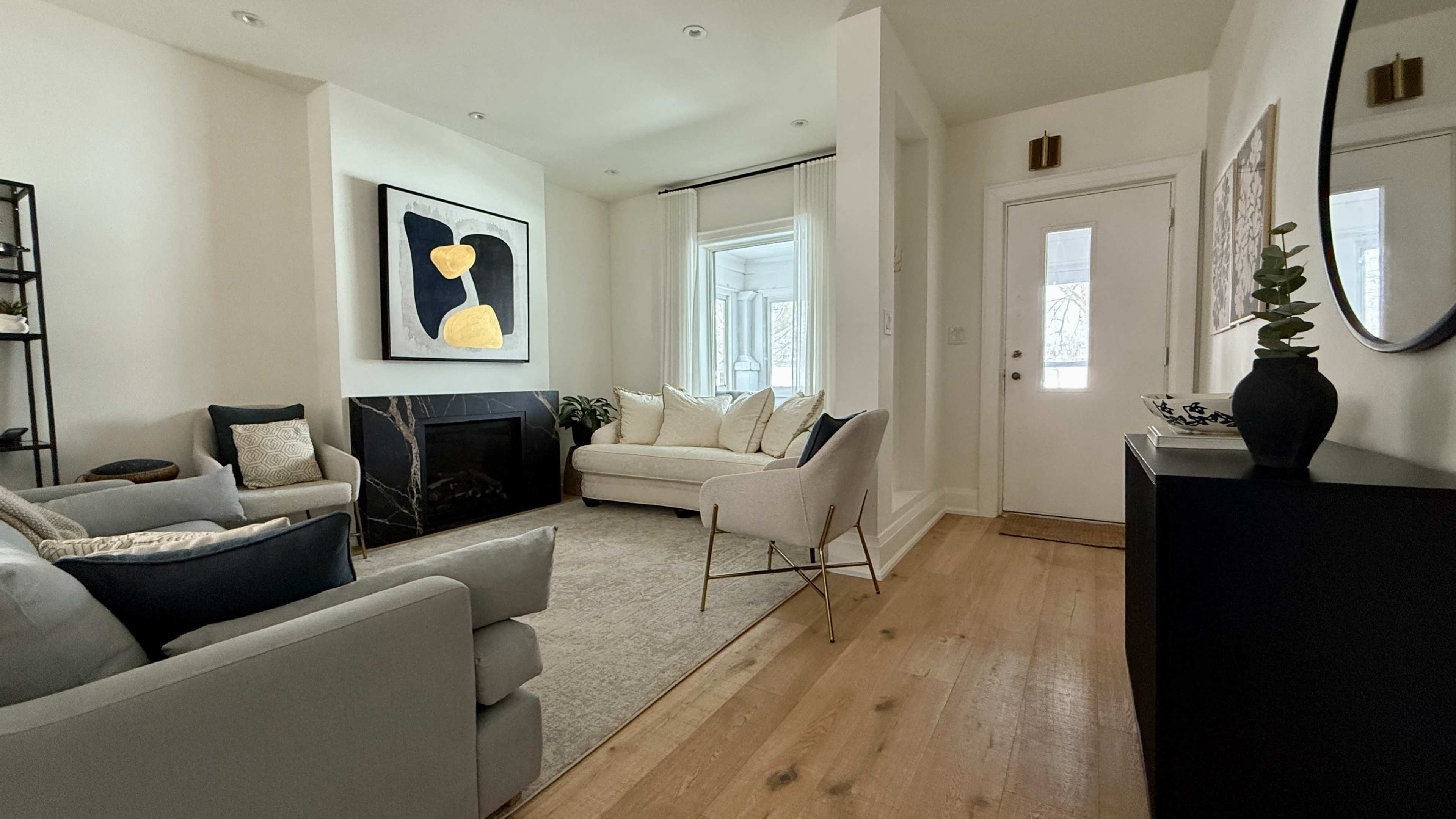 The image shows a modern living room with a light-colored sofa, a fireplace, a large abstract painting on the wall, and a door leading outside.