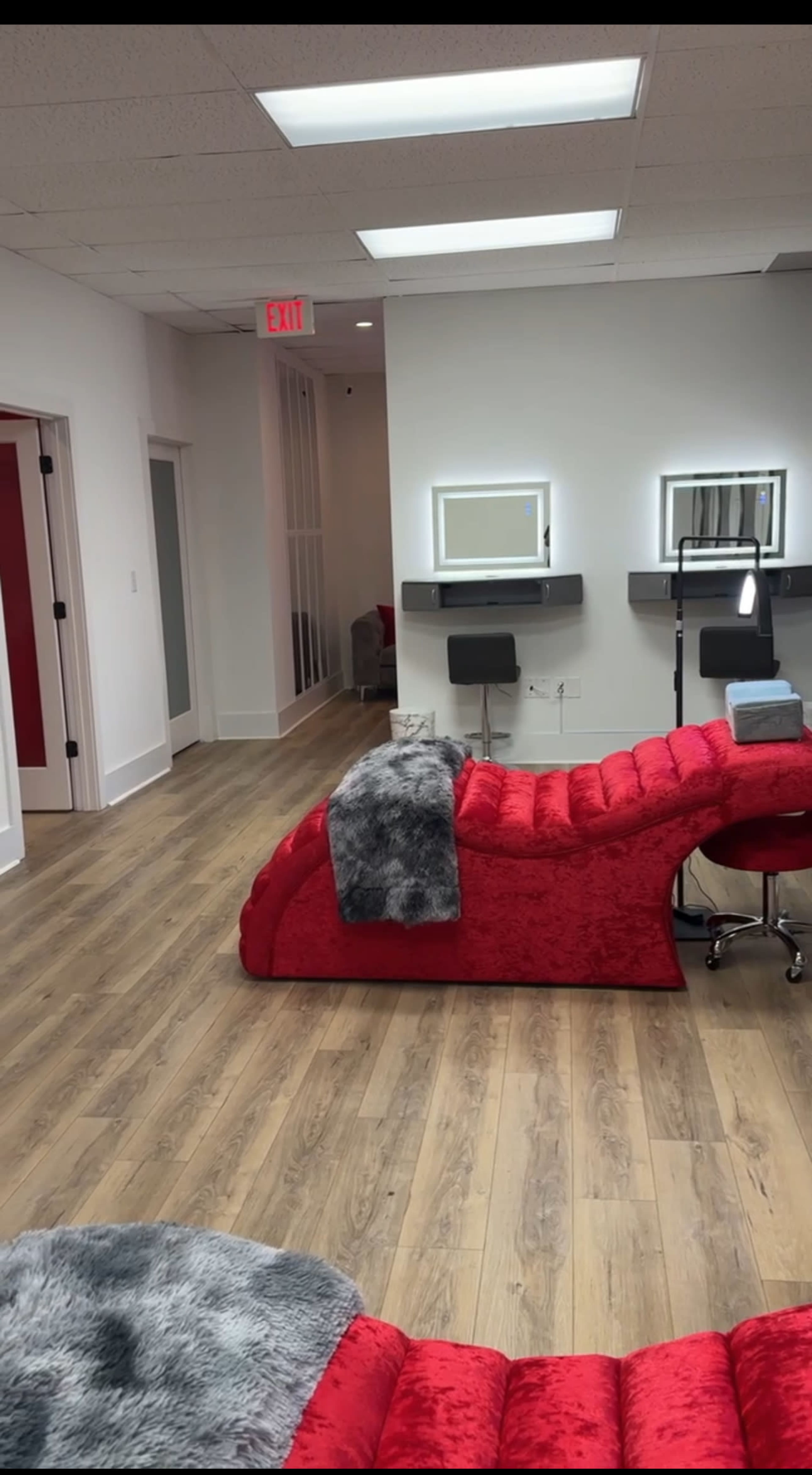 The image shows a modern salon interior featuring a red reception area with a plush chair and two mirrors mounted on the wall.