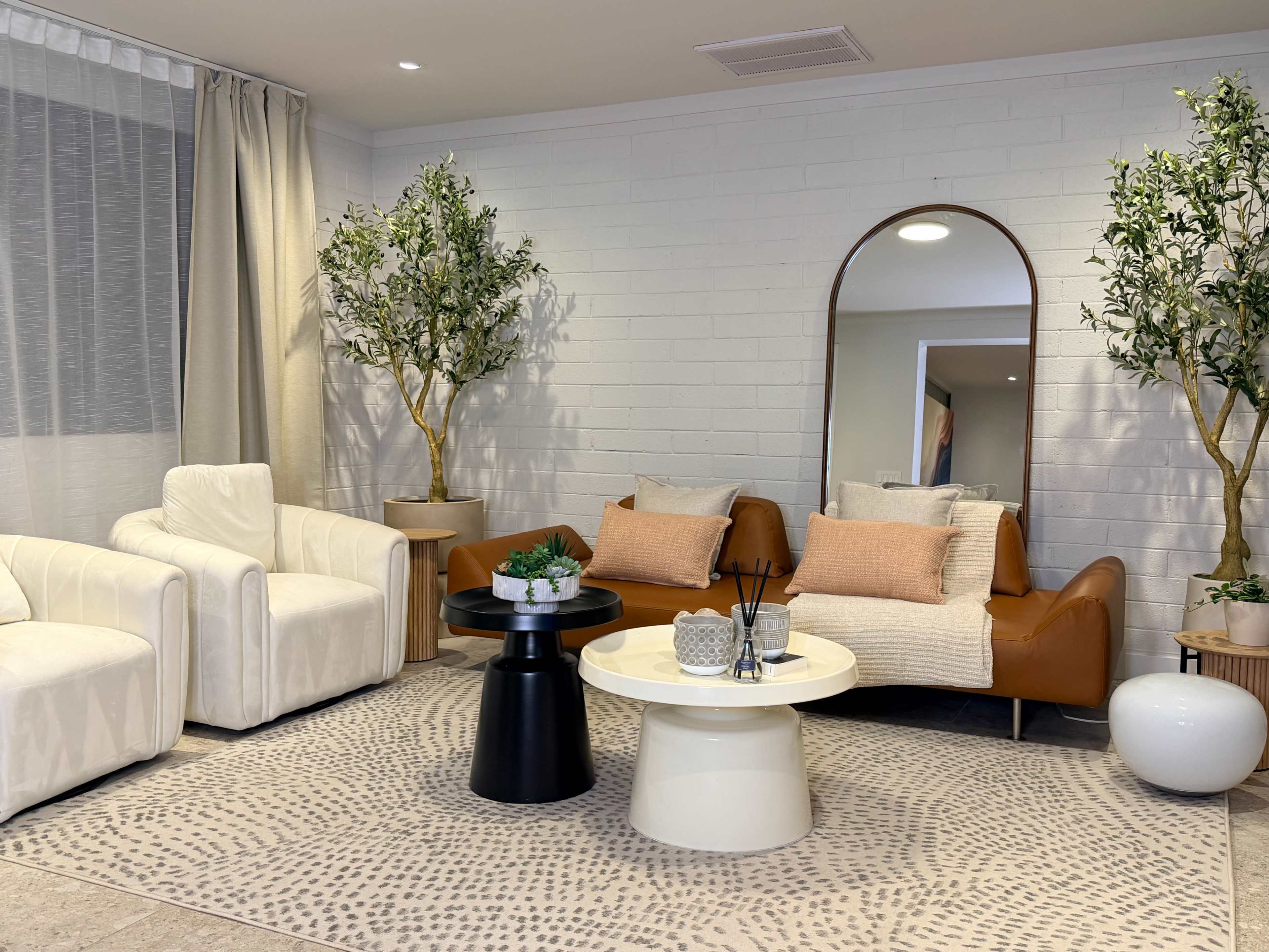 The image shows a modern living room with two armchairs, a coffee table, and decorative elements such as plants and a large mirror.