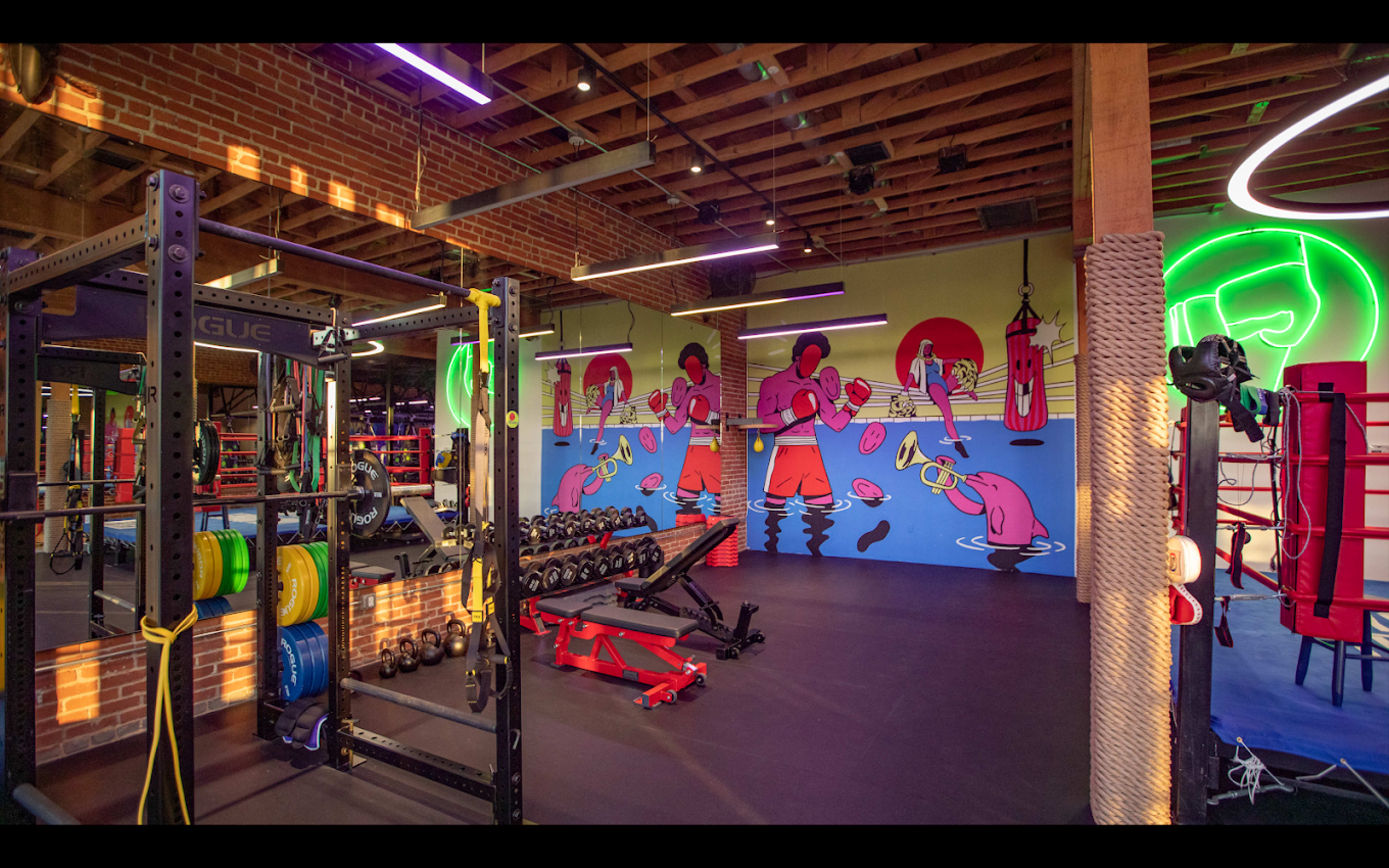 A brightly lit gym with colorful murals, weightlifting equipment, and a boxing area featuring punching bags.