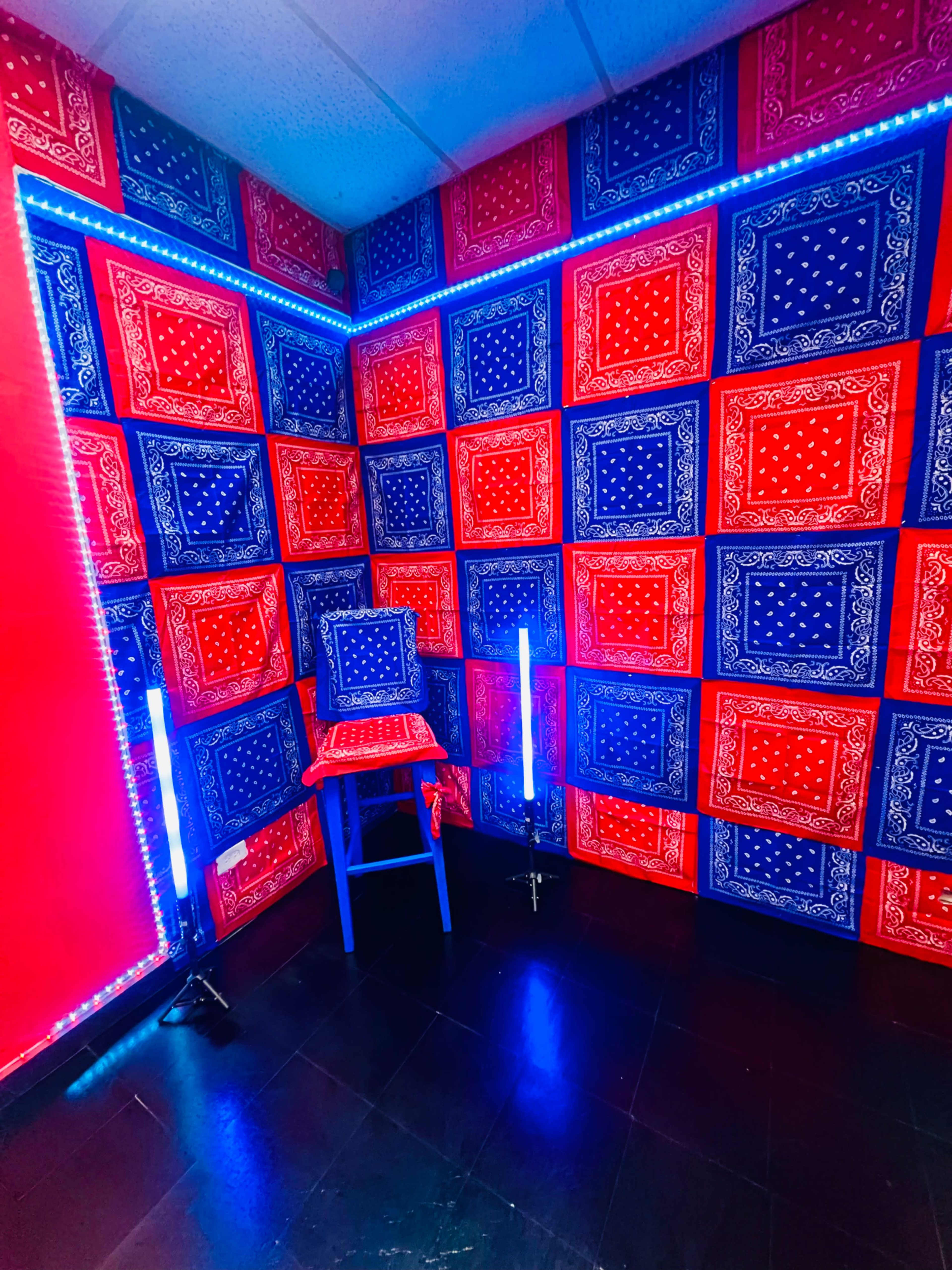 The image shows a corner of a room decorated with red and blue bandana-patterned wallpaper, a matching table, and neon lights.