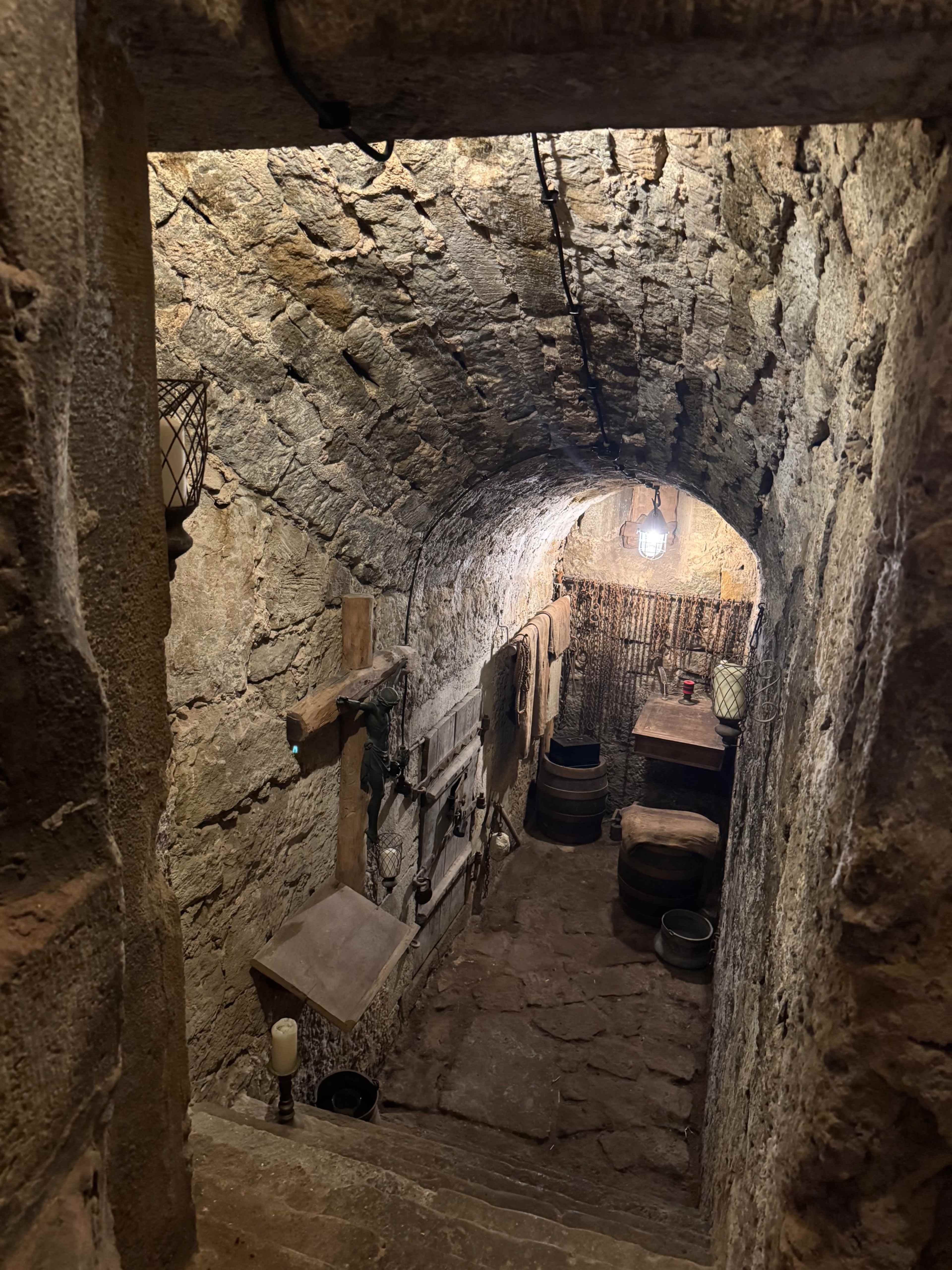 The image shows a dimly lit stone cellar with a wooden table, barrels, and various tools along the walls.