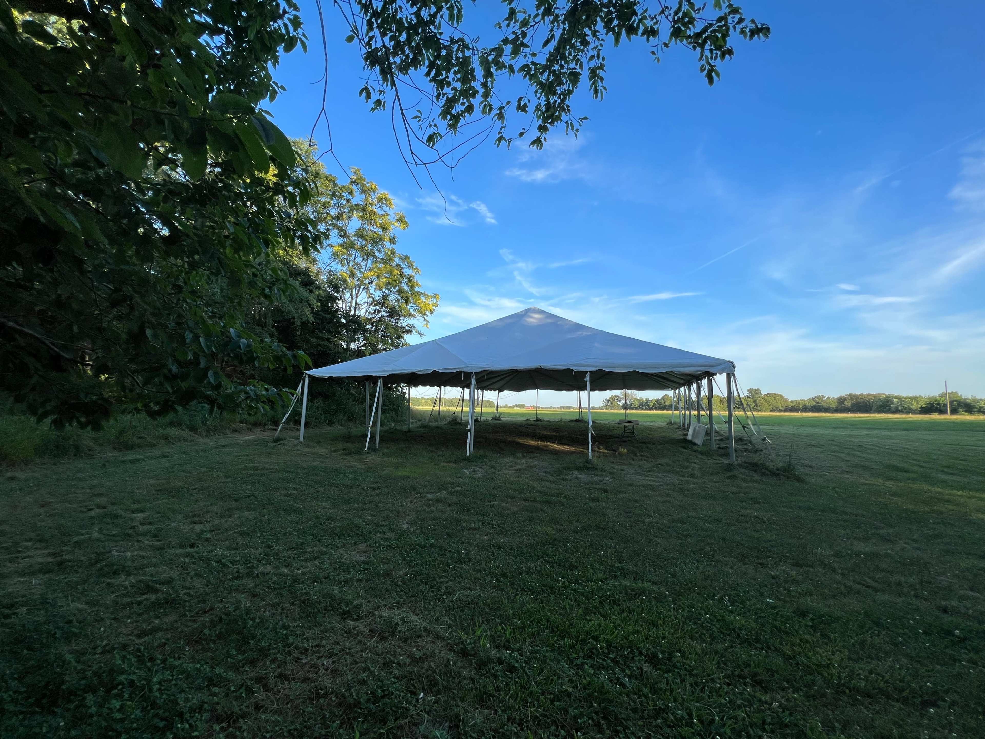 A large white tent is set up on a grassy field under a clear blue sky.