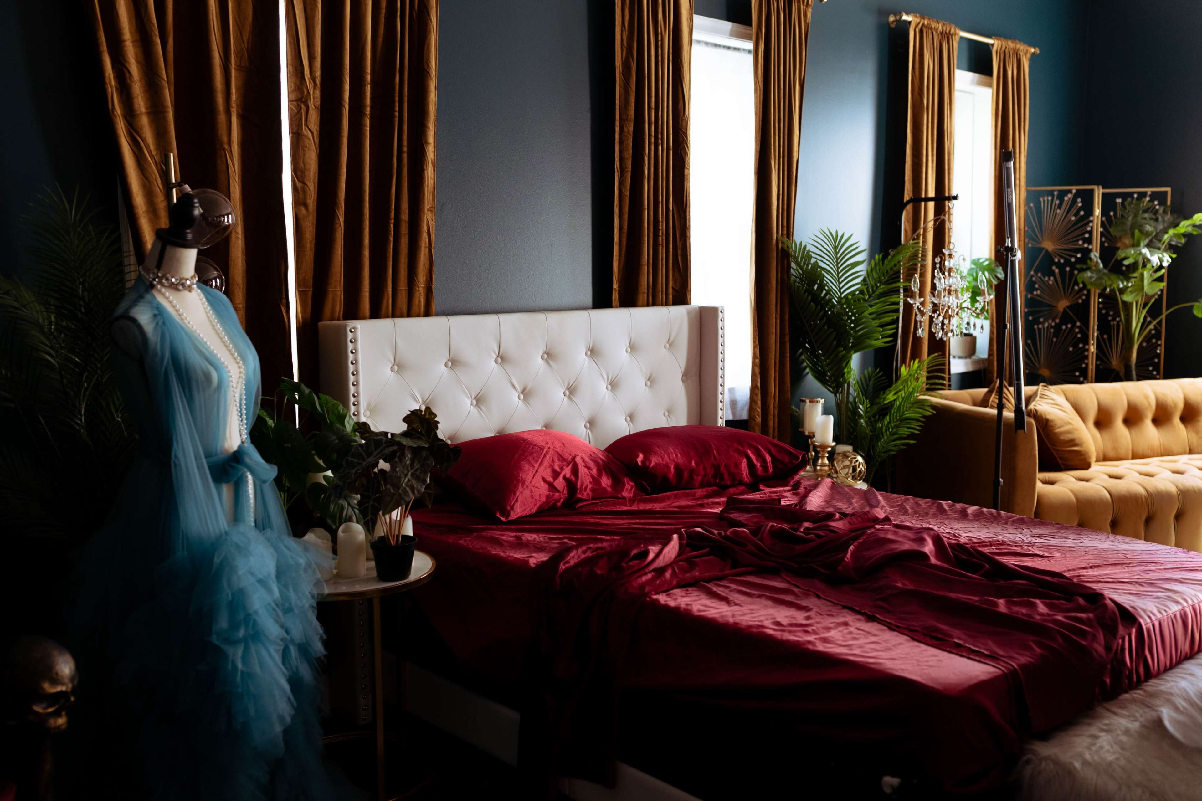The image shows a neatly arranged bedroom with a large bed covered in red bedding, flanked by elegant curtains and a stylish couch.