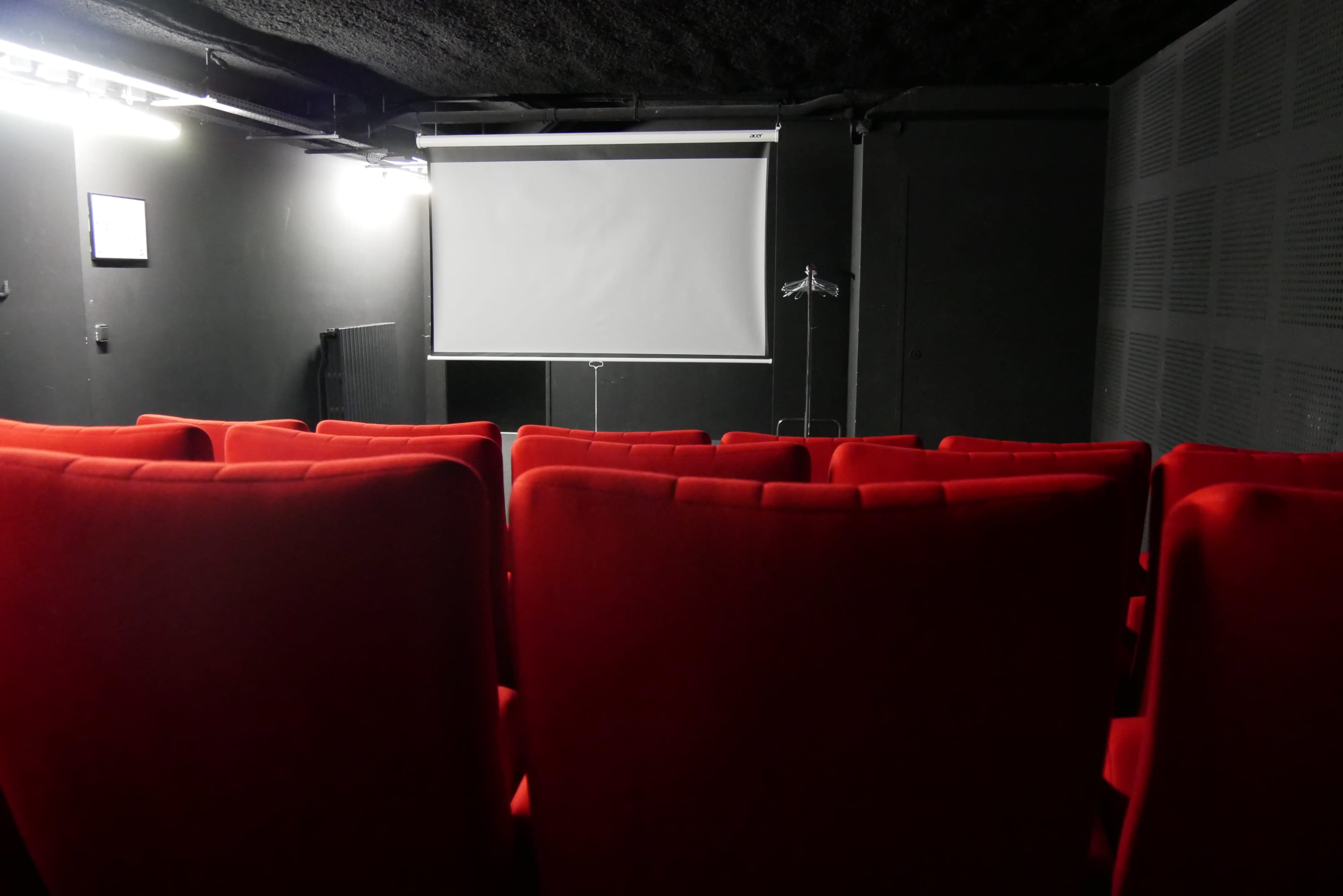 An empty small theater with red seating facing a blank white projection screen.