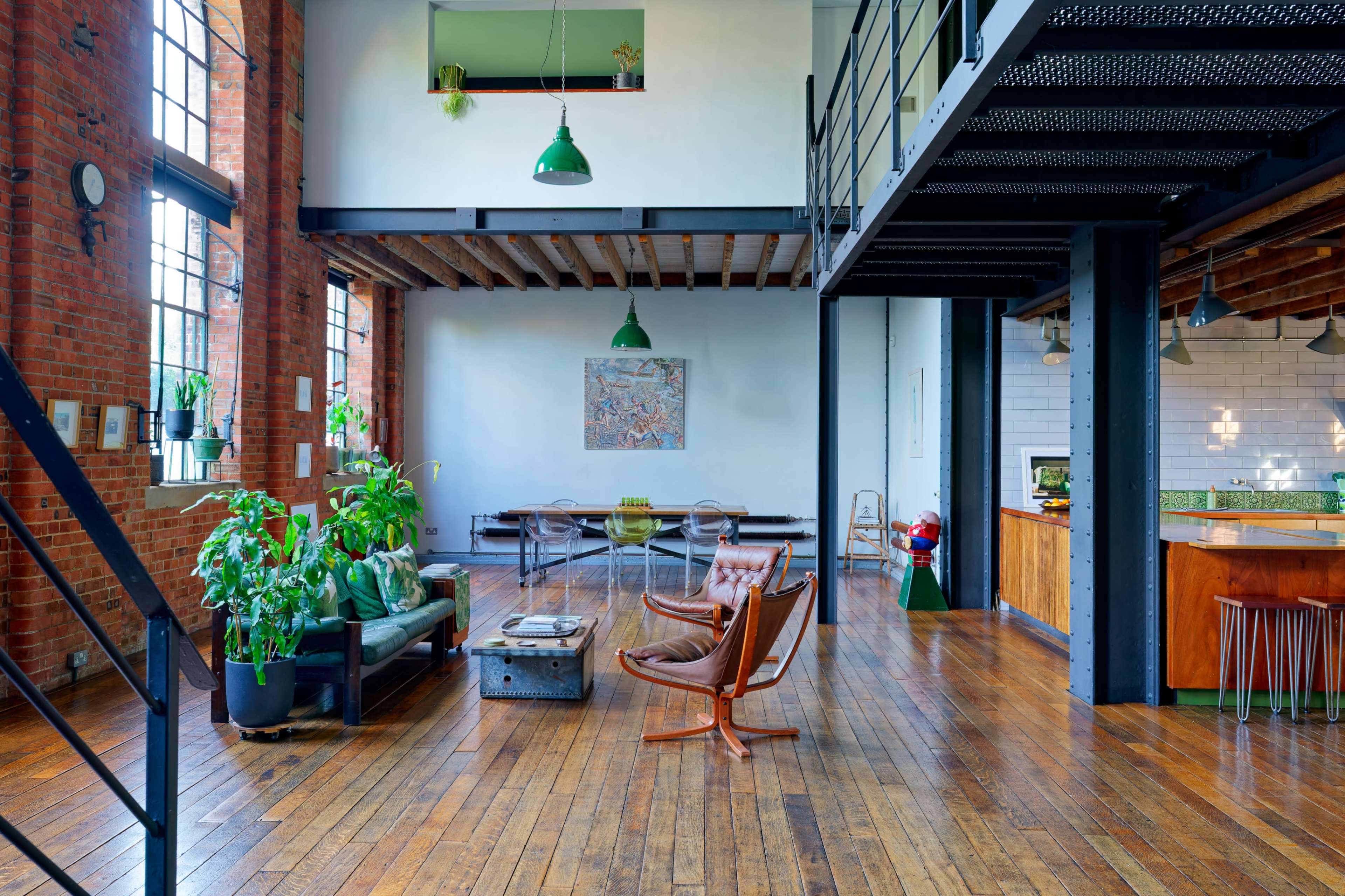 The image shows a spacious, industrial-style loft featuring wooden floors, exposed brick walls, and modern furniture arranged around a central living area.