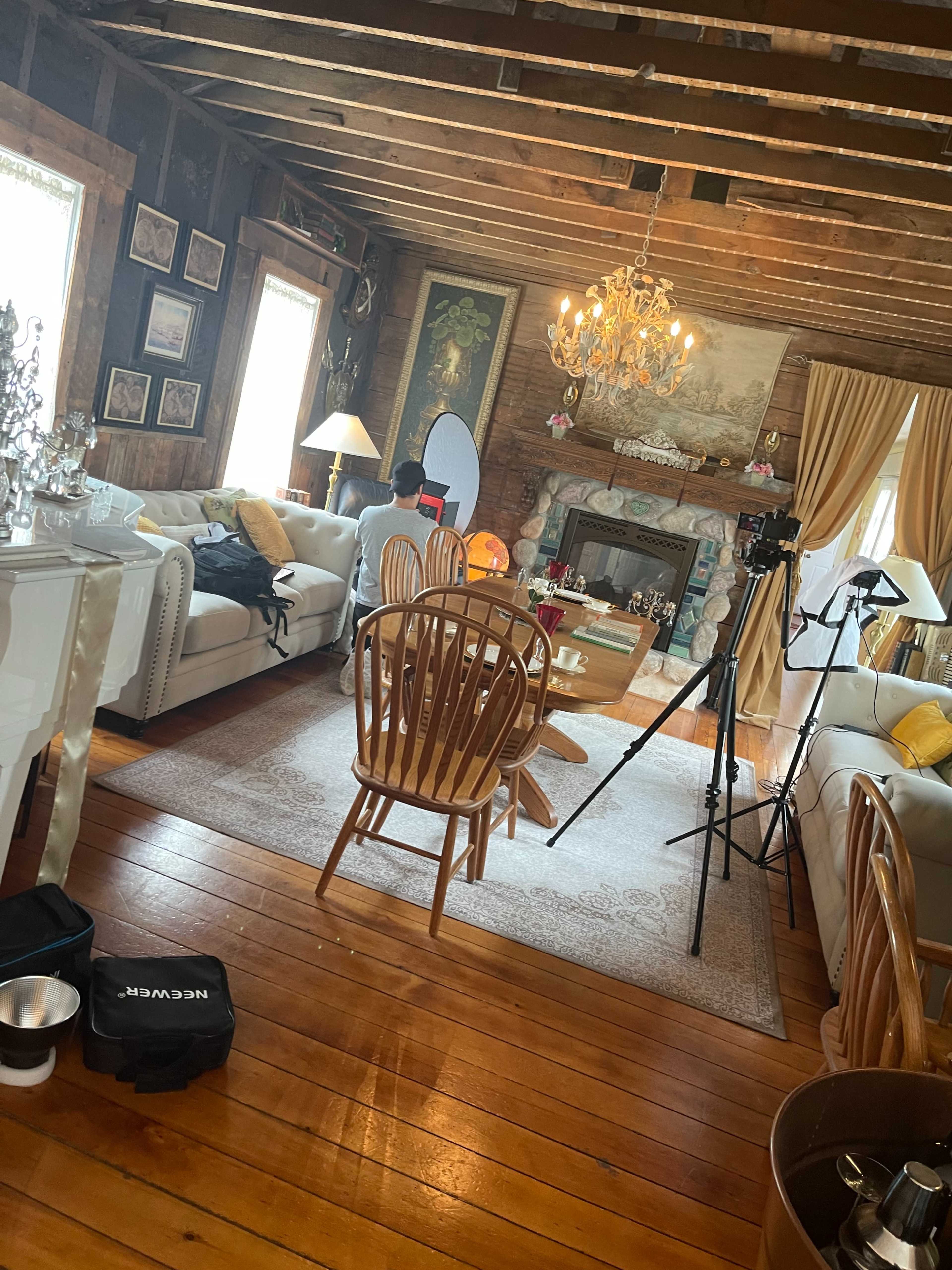 A cozy living room with wooden floors, a chandelier, and a seating area featuring white sofas and a coffee table, along with a camera setup.
