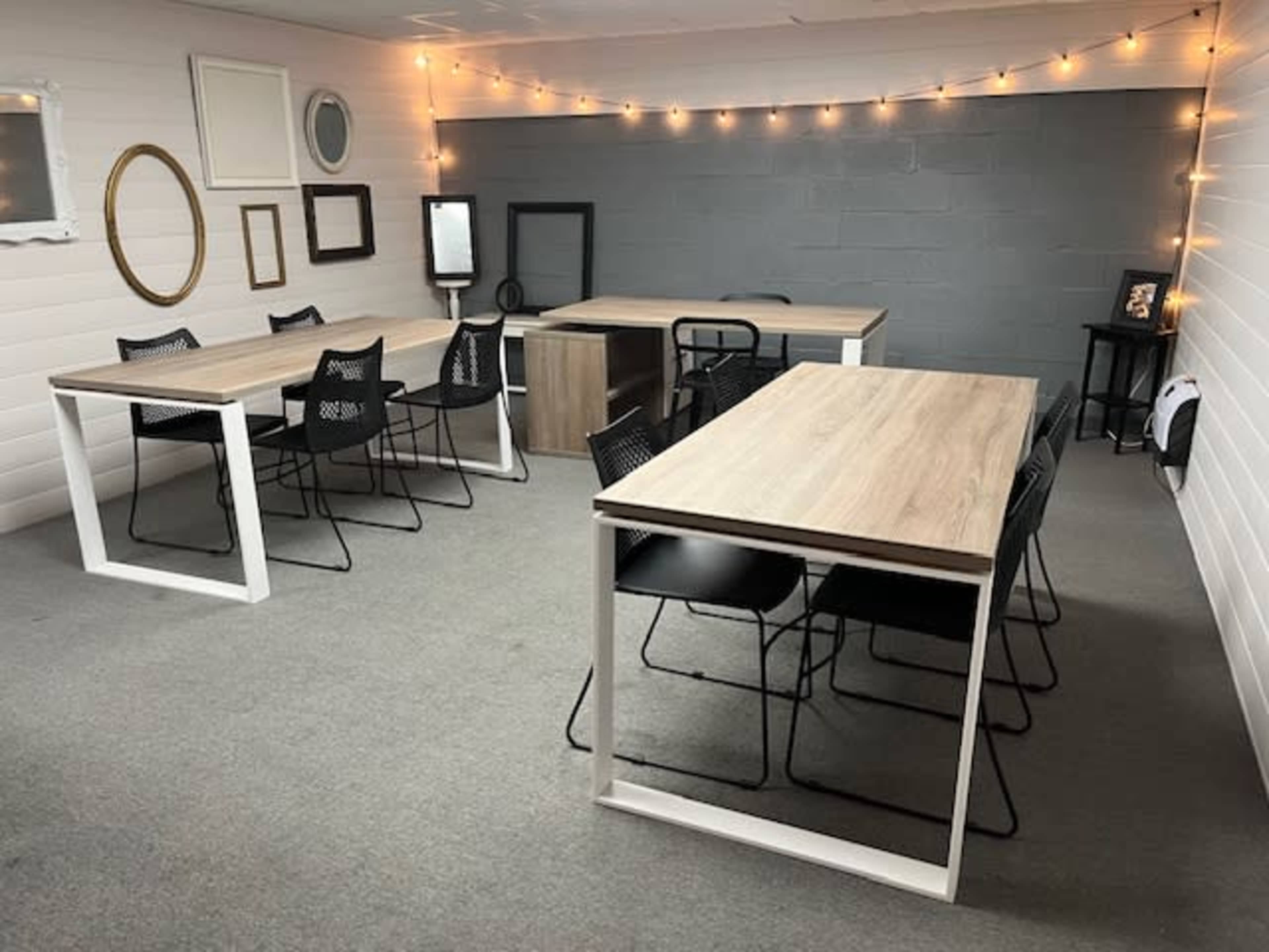 A spacious room features multiple tables surrounded by chairs, with string lights illuminating the gray walls.