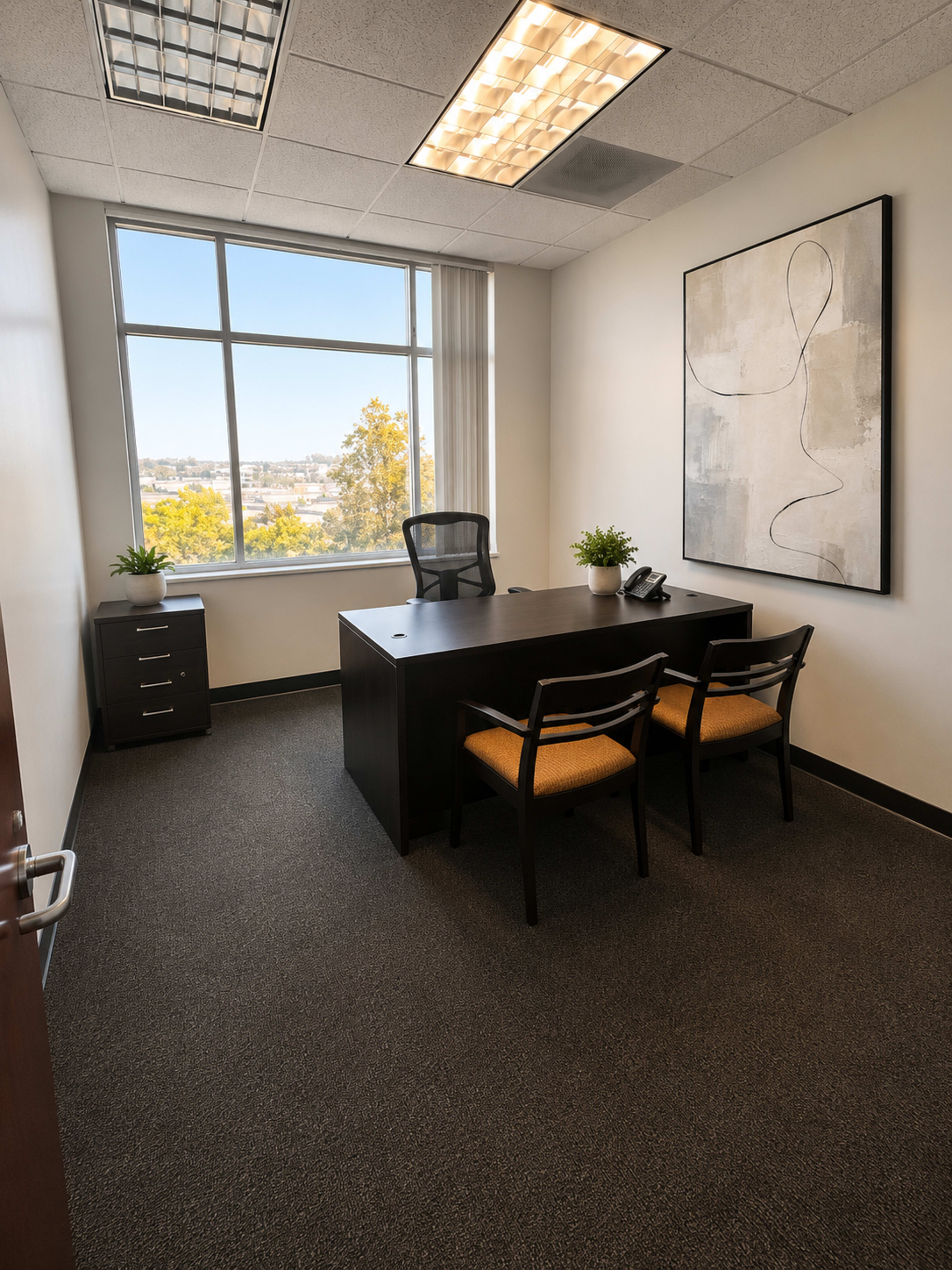 The image shows a small office with a desk, two chairs, a filing cabinet, and a large window featuring a view of trees outside.