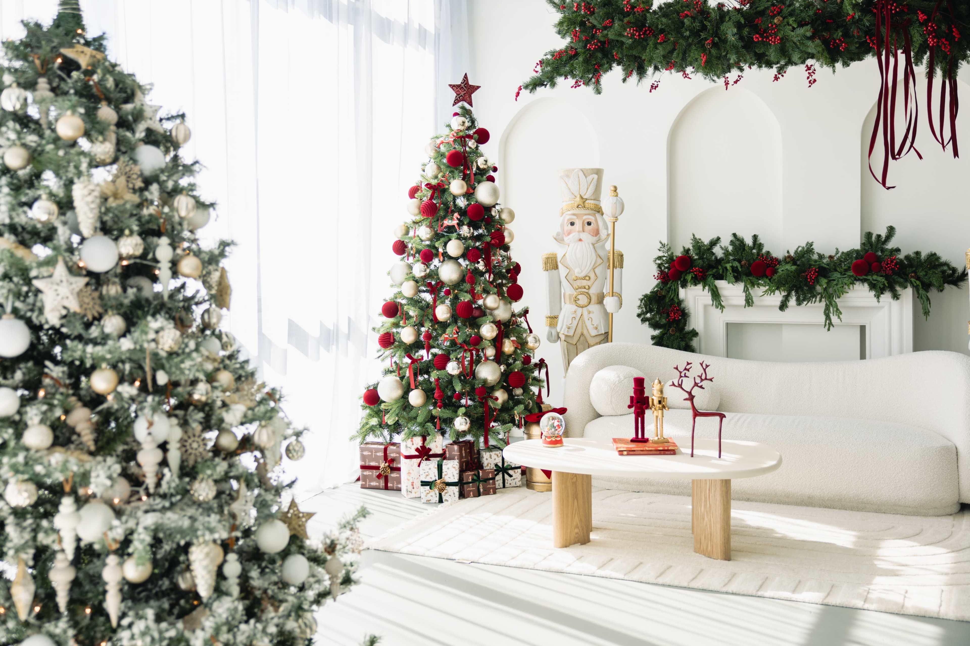 The scene features a brightly decorated living room with two Christmas trees, a white sofa, and festive ornaments, all set against a backdrop of greenery and holiday accents.