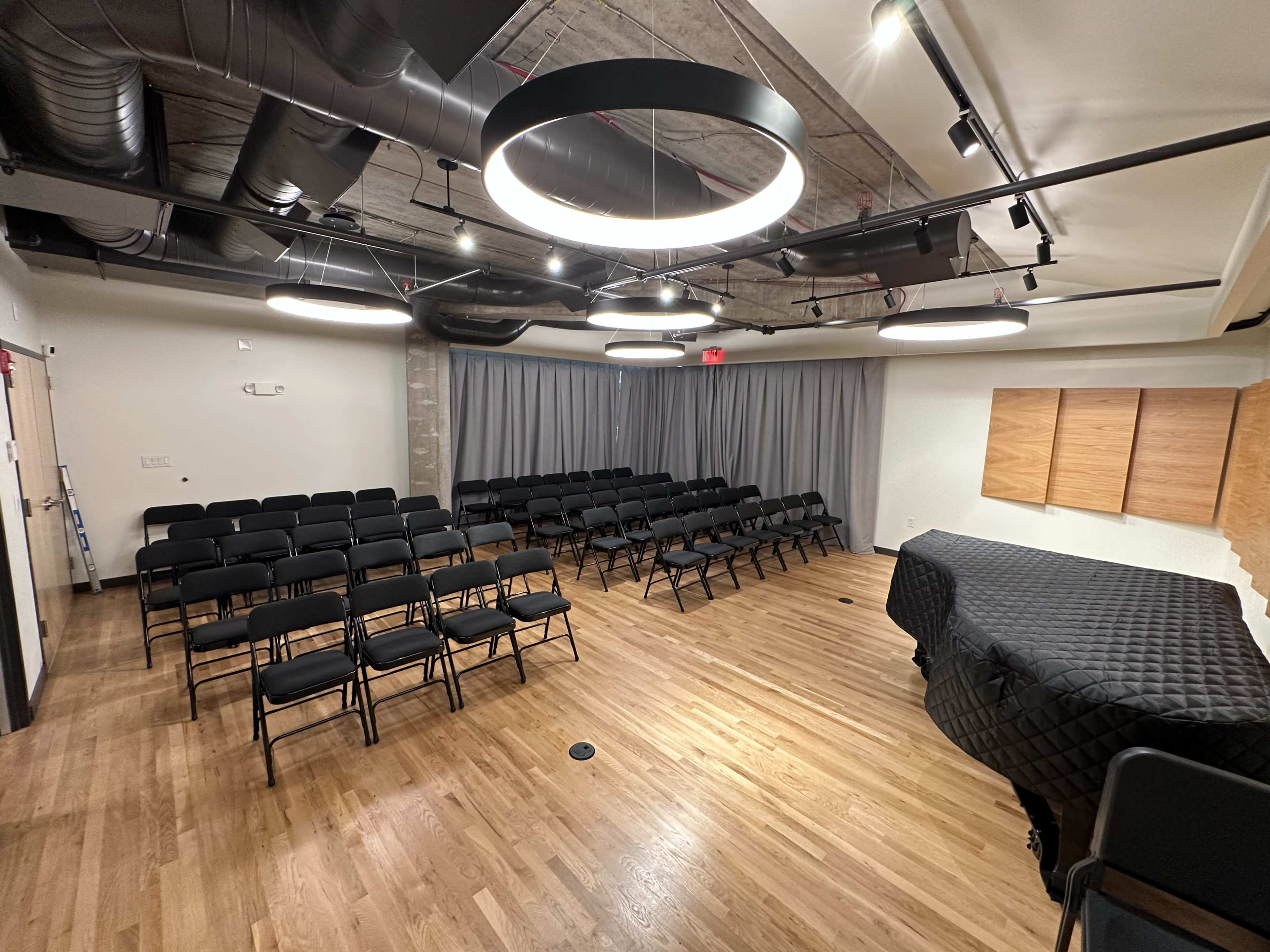 A newly designed meeting room with rows of black chairs facing a stage, equipped with modern lighting and wooden wall panels.